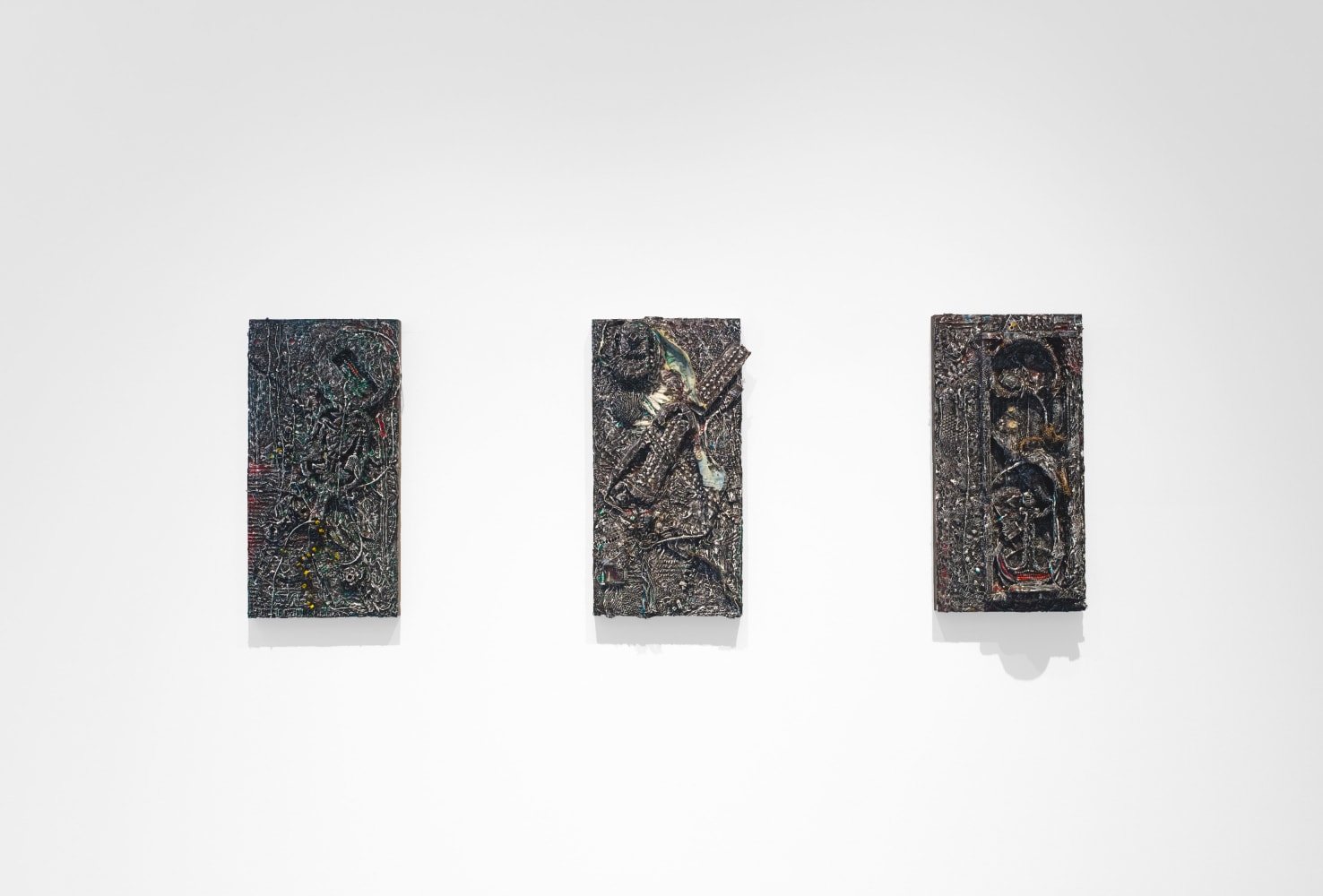 Three small, textured, and dark artworks of the same size hang on gallery wall.