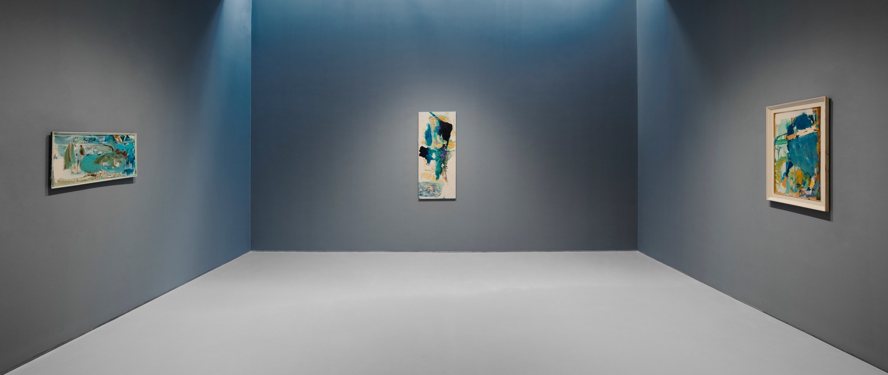 Three abstract paintings placed on separate adjacent blue walls