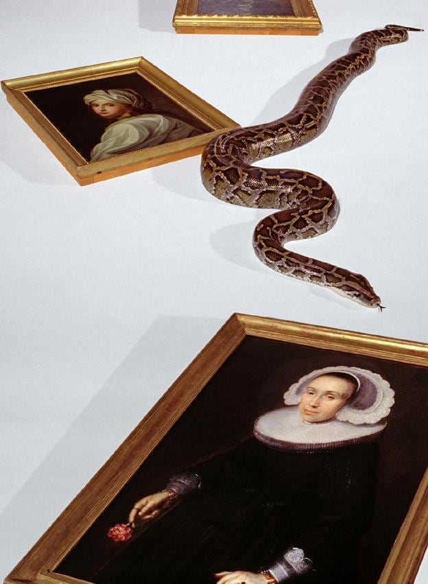 a snake slithers between several portrait paintings in gilt frames