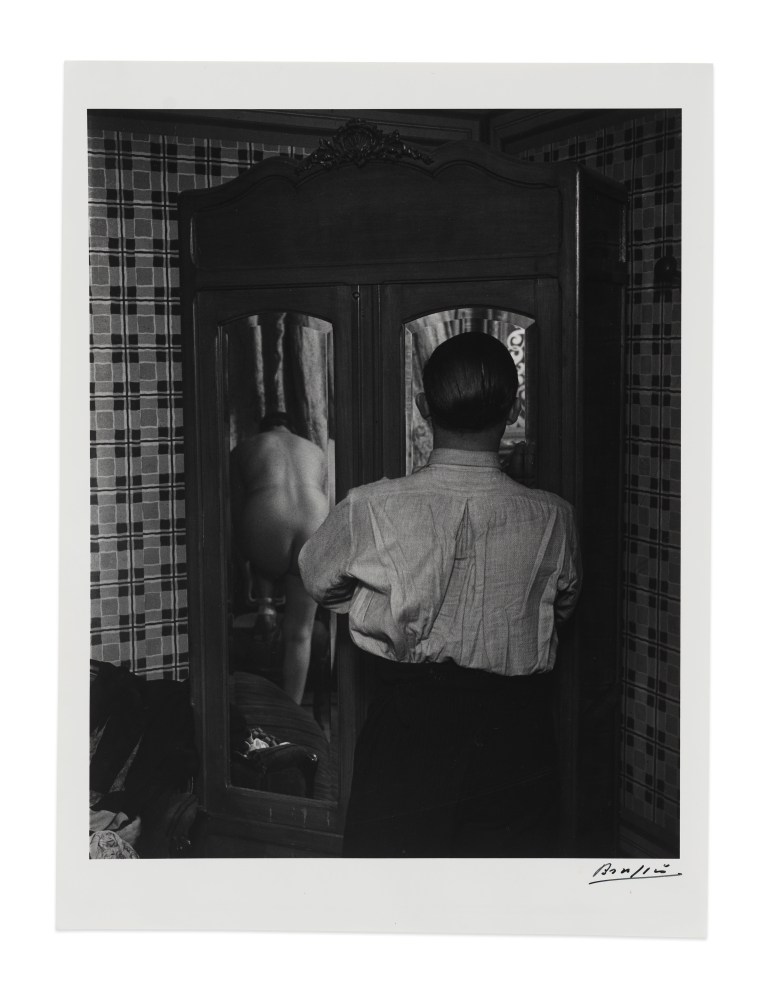 Black and white silver gelatin print of man looking into mirrored wardrobe in a brothel by Brassaï