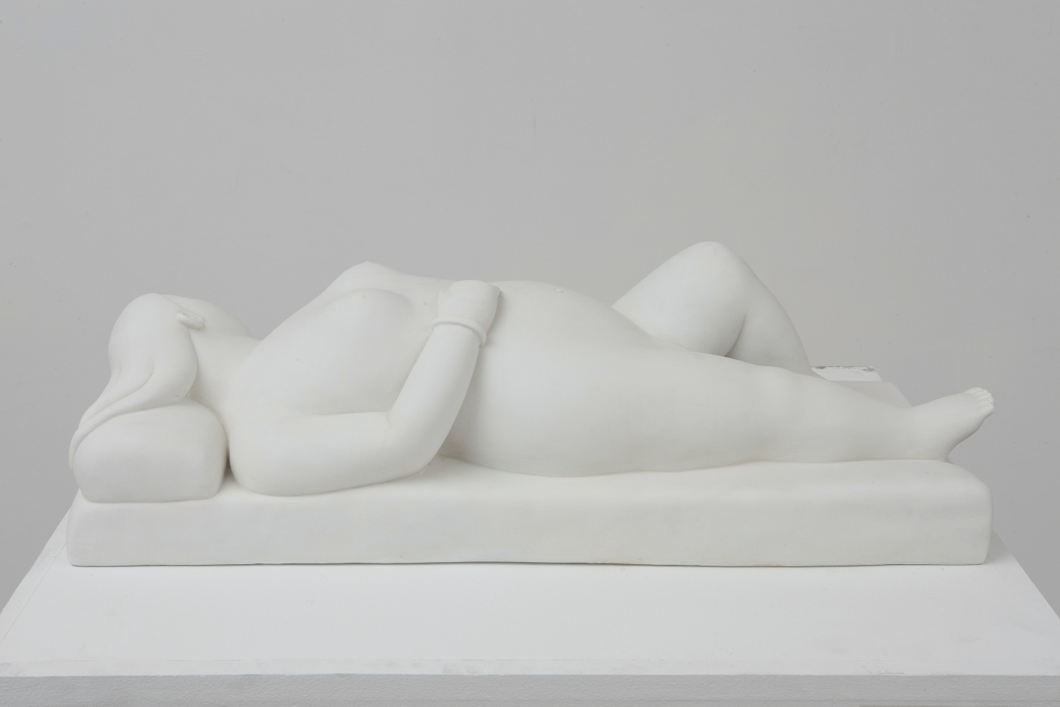 White marble sculpture of a reclining woman on pillow.