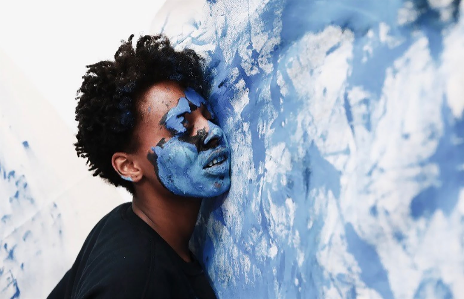 Photo of a woman with blue paint on her face pressing her face into a canvas