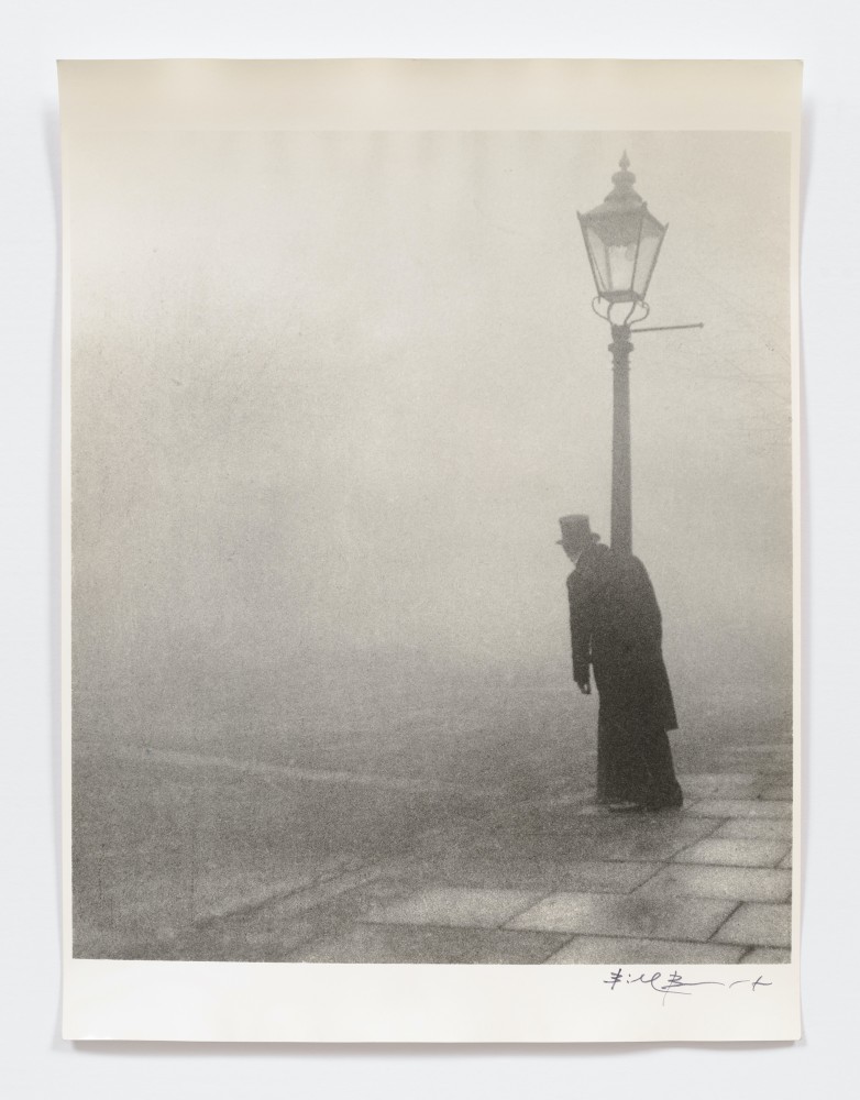 Black and white silver gelatin print of man leaning on lamp post in fog.
