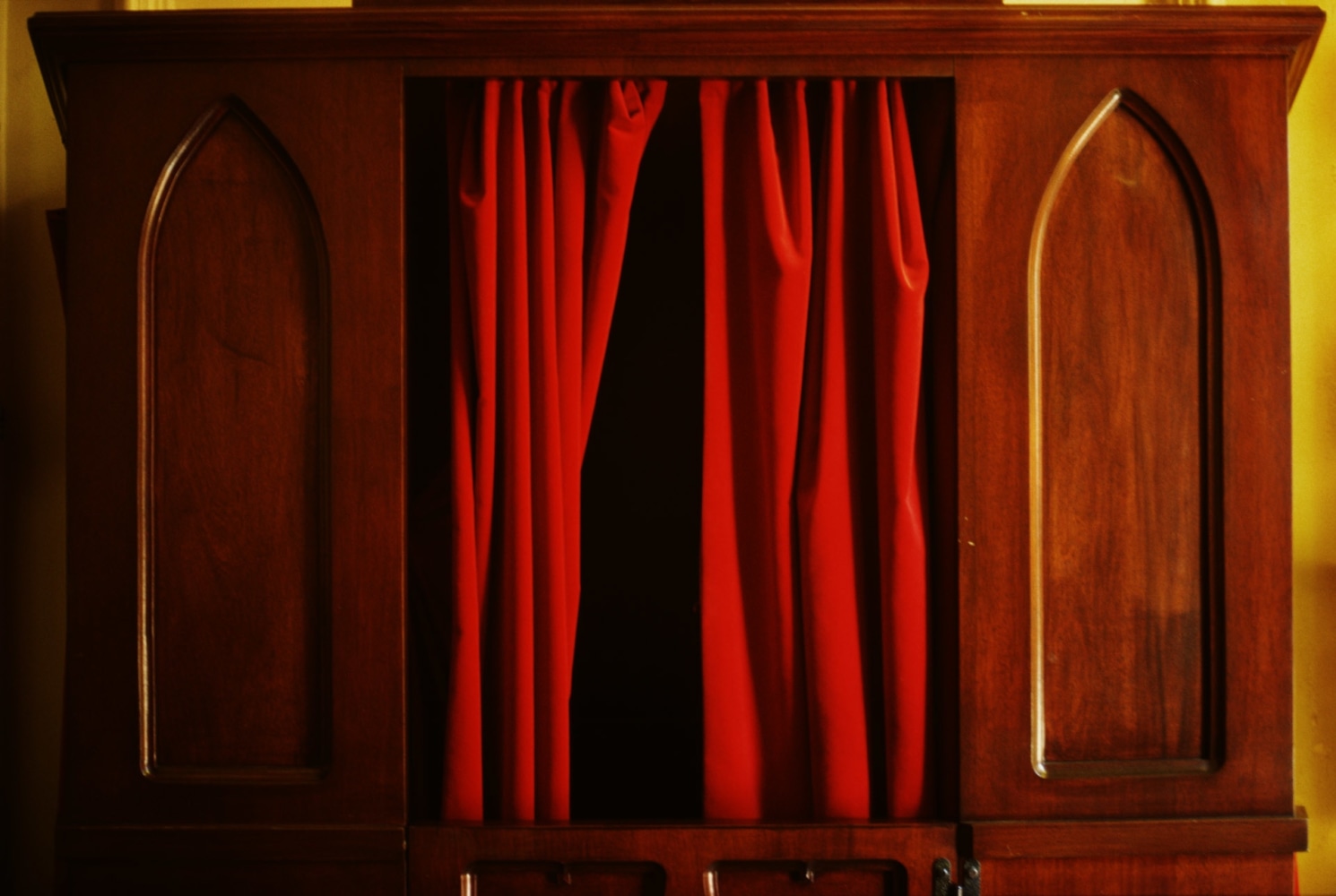 Image of a confessional booth with a red curtain, half pulled back, by Mickey Aloisio