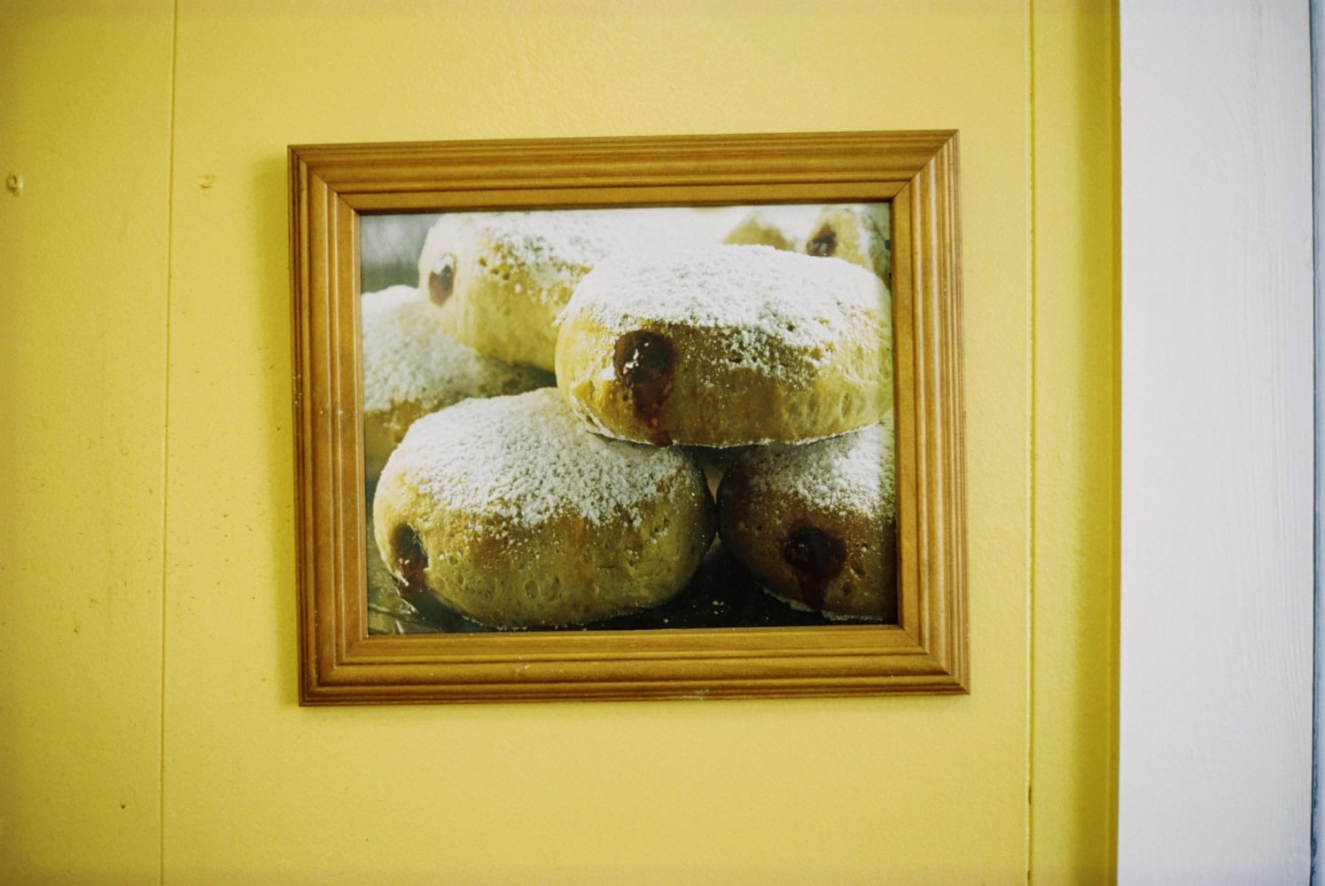 Image of a yellow wall and framed photograph of powdered jelly donuts by Mickey Aloisio