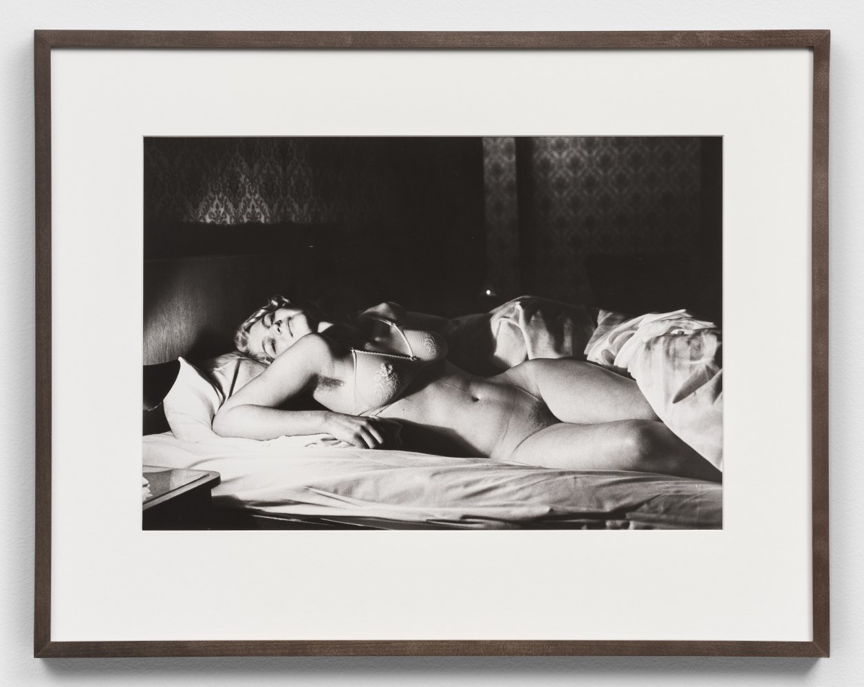 Black and white photographic print by Helmut Newton of a nude woman in bed