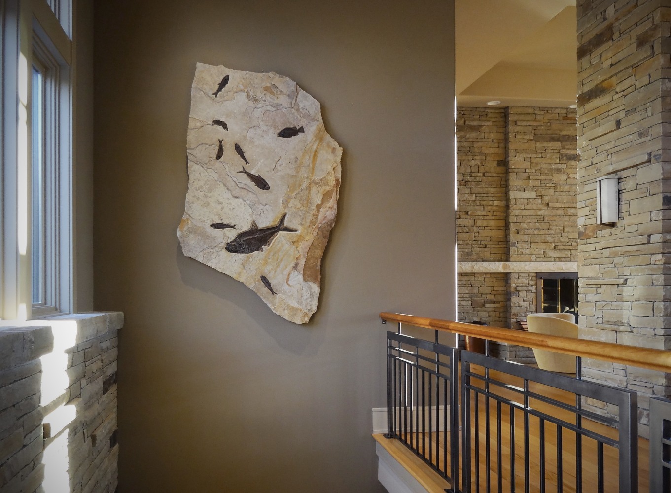 An irregularly shaped fossil mural containing large and small fossil fish hangs in a room with similarly colored stone tiles