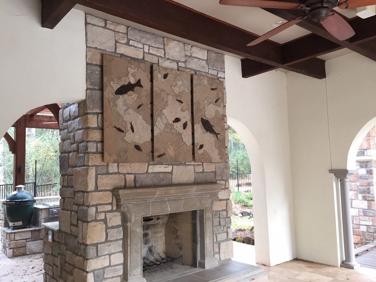A fossil triptych containing large and small fossil fish sits above a covered outdoor firelace