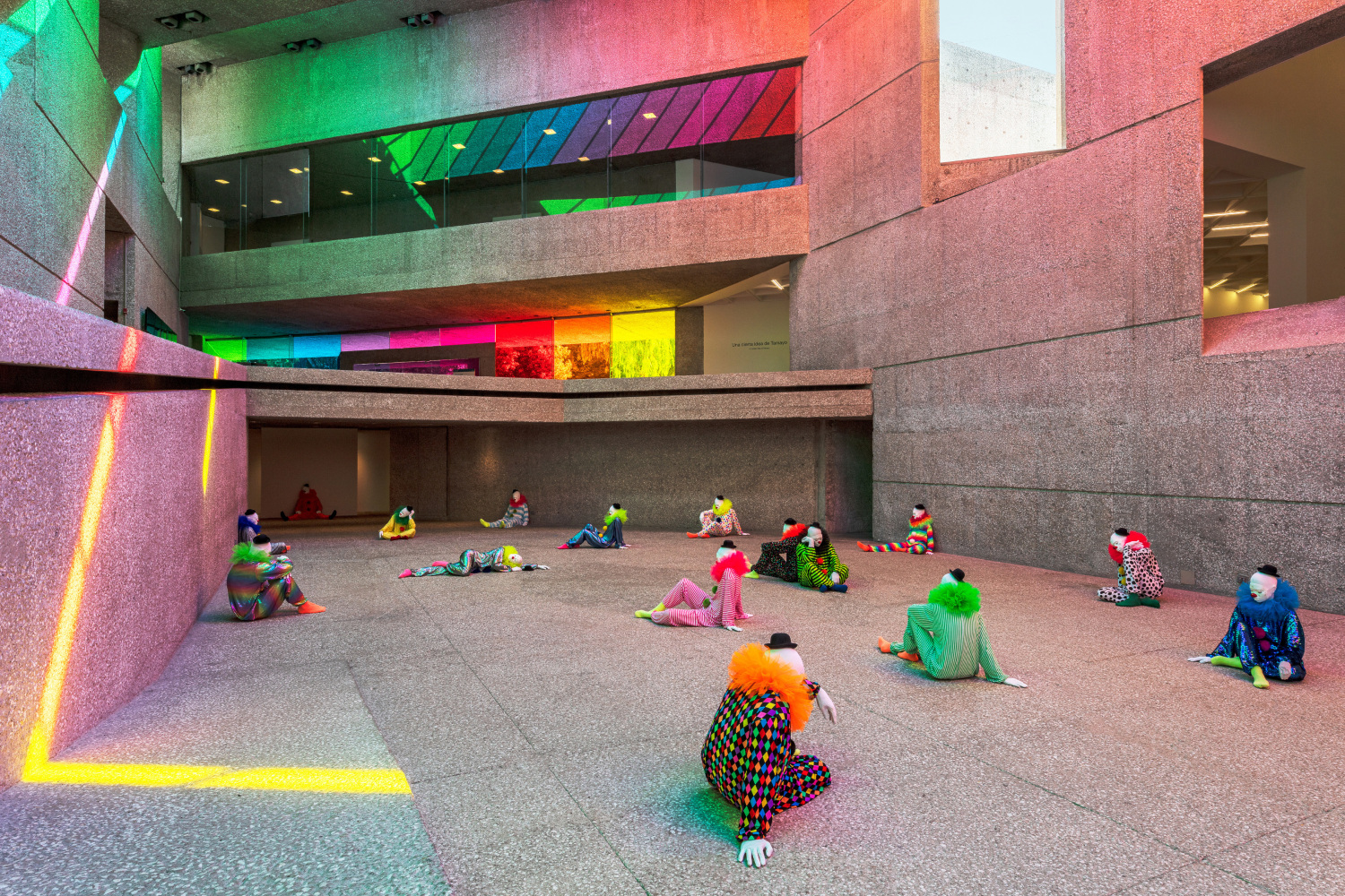 Installation view of colorful clown sculptures and rainbow colored windows by Ugo Rondinone
