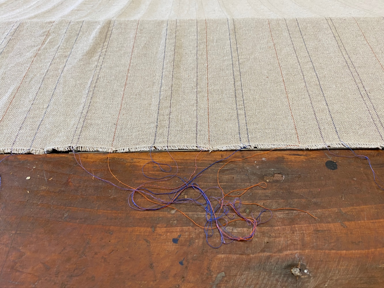 Color photograph of a textile based artwork comprised of a large rectangular piece of tan linen draped over a trap door opening in the floor. Artwork by Gabriela Salazar, installed at the Al Held Foundation, 2021. Exhibition curated by Olga Dekalo and River Valley Arts Collective.