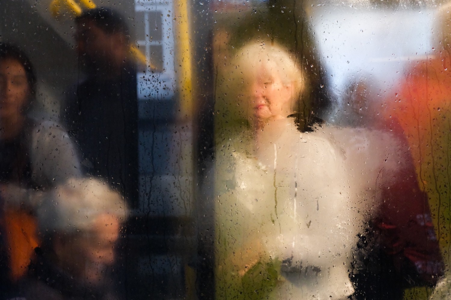 a photograph that looks like a watercolor of a woman sitting on a bus with rain on the window
