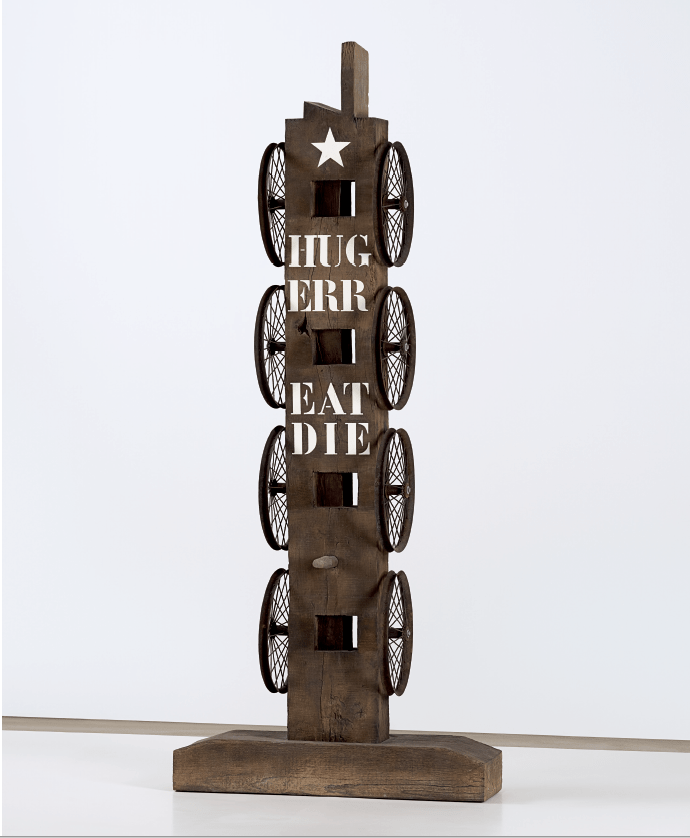 A beam sculpture with a haunched tenon. Four wheels are arranged vertically on each side of the sculpture. At the top of the front of the sculpture is a white star, below that the words Hug, Err, Eat, and Die
