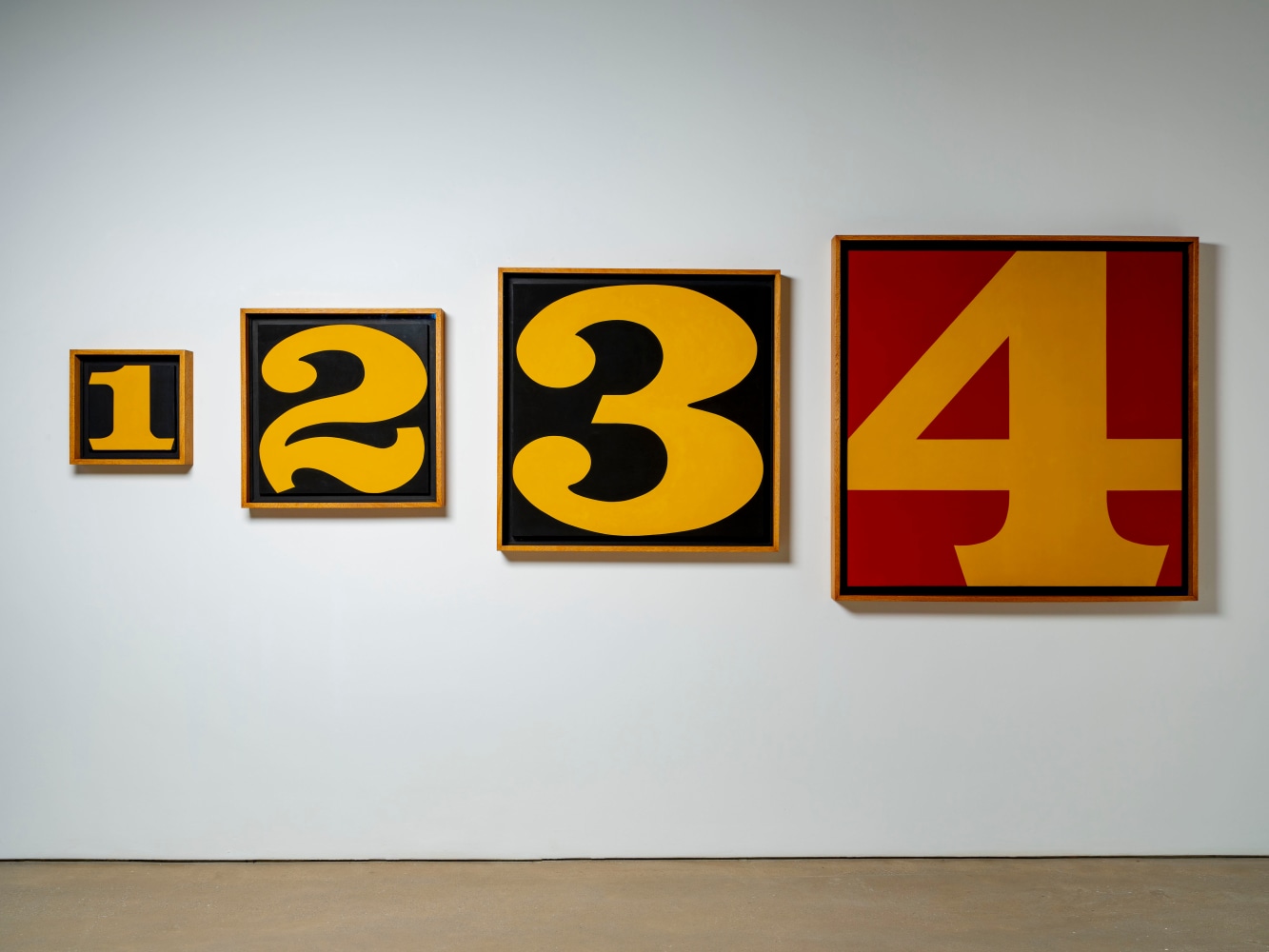 Indiana's Exploding Numbers, four canvases, the first and smallest with a yellow numeral one on a black background, followed by a larger yellow numeral two on a black background, and a yellow numeral three on a black background. The largest canvas is a yellow numeral four on a red background.