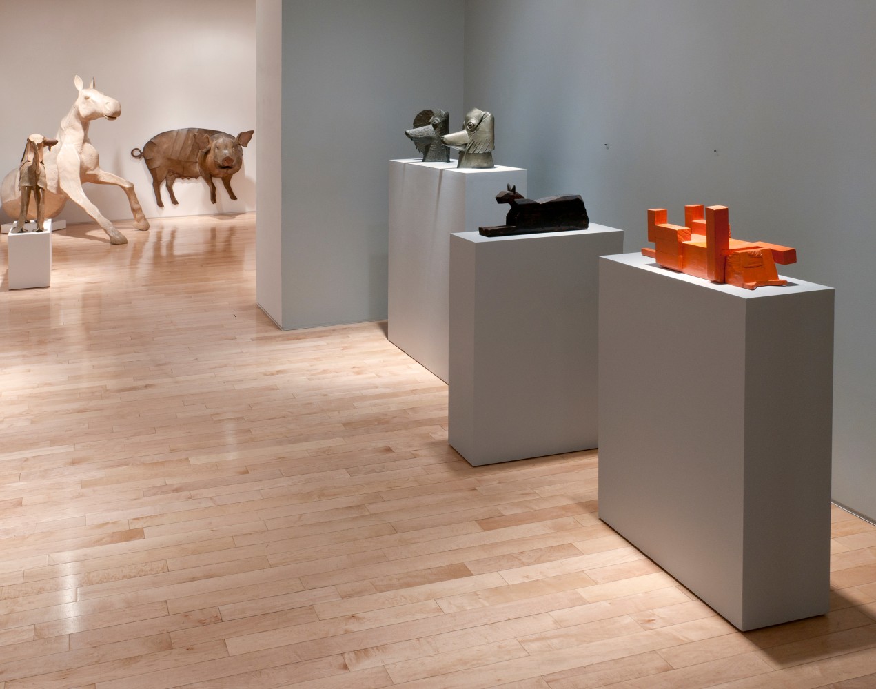 Photograph showing a view of an exhibition space, with various sculpture on pedestals and one hanging from the wall