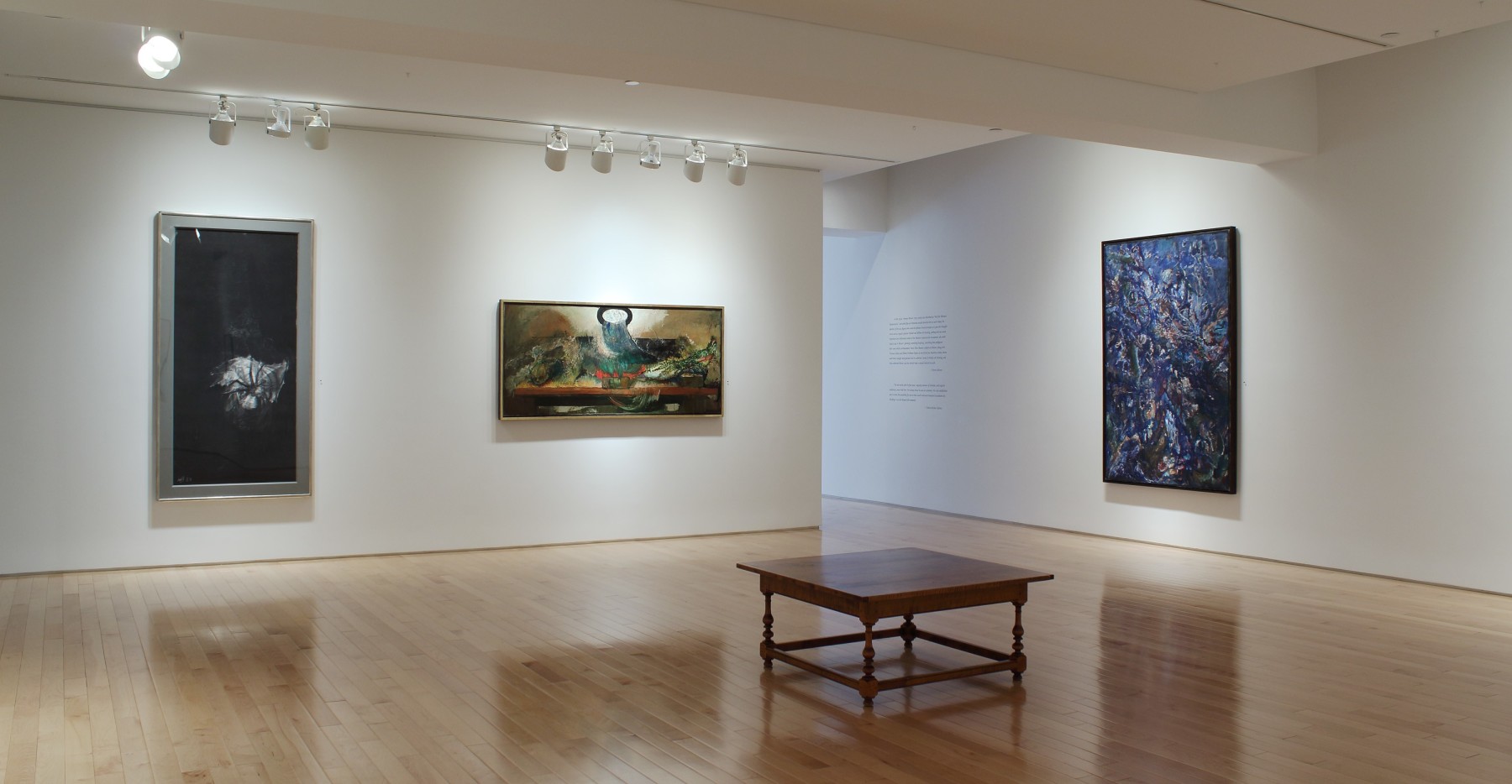 Photograph showing a corner view of an exhibition space with three paintings hanging on white walls