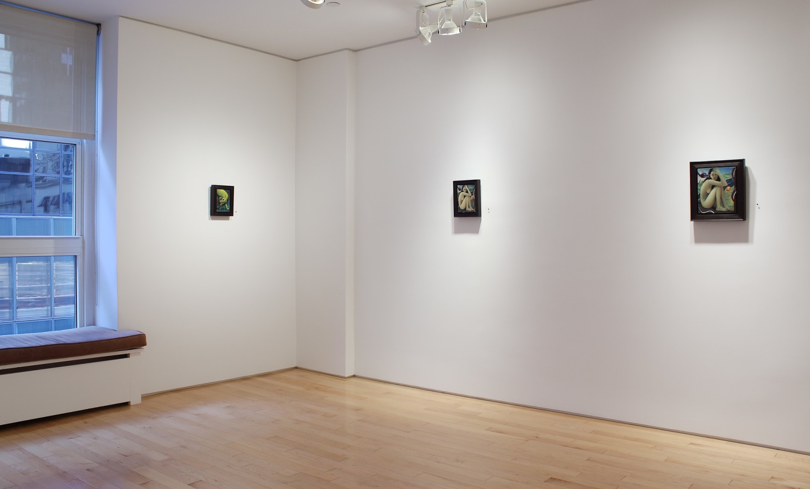 Photograph showing a view of a corner view of an exhibition with three small paintings hanging on white walls