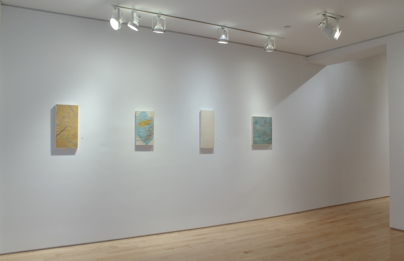 Photograph showing a corner view of an exhibition space, with four paintings hanging on white walls