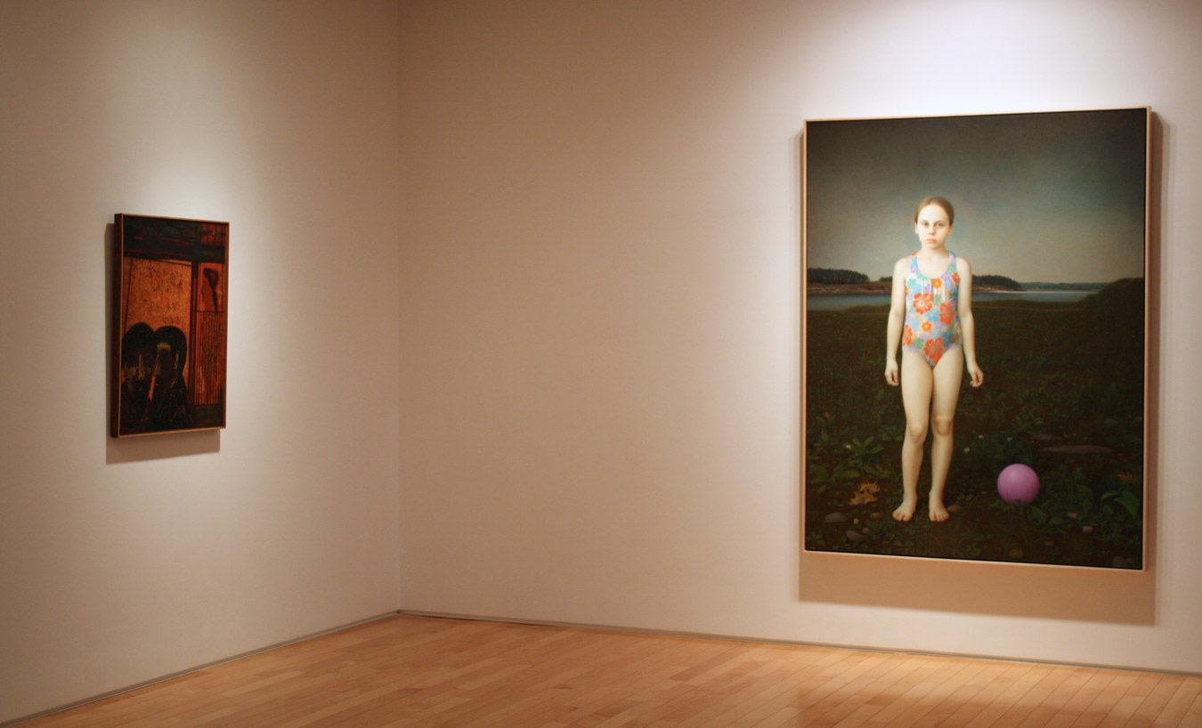 Photograph showing a corner view of an exhibition space, with two framed paintings hanging on white walls