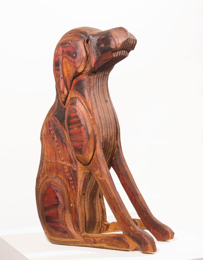Wood sculpture of a dog sitting on its hind legs