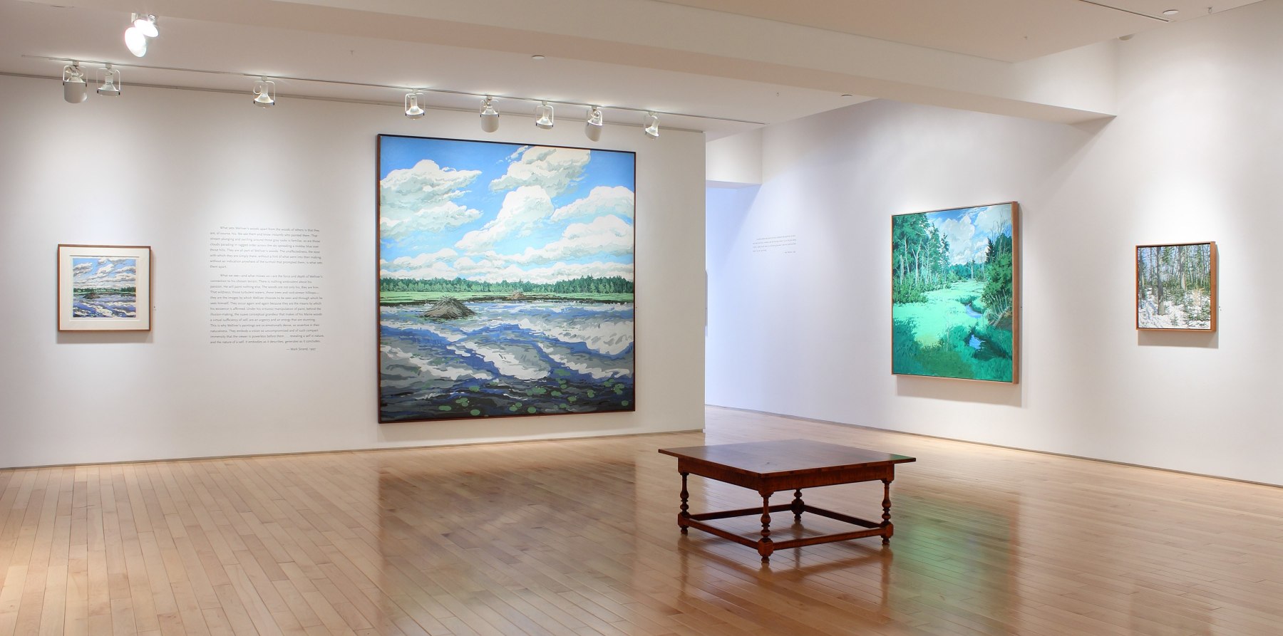 Photograph showing a corner view of an exhibition with four paintings hanging on white walls