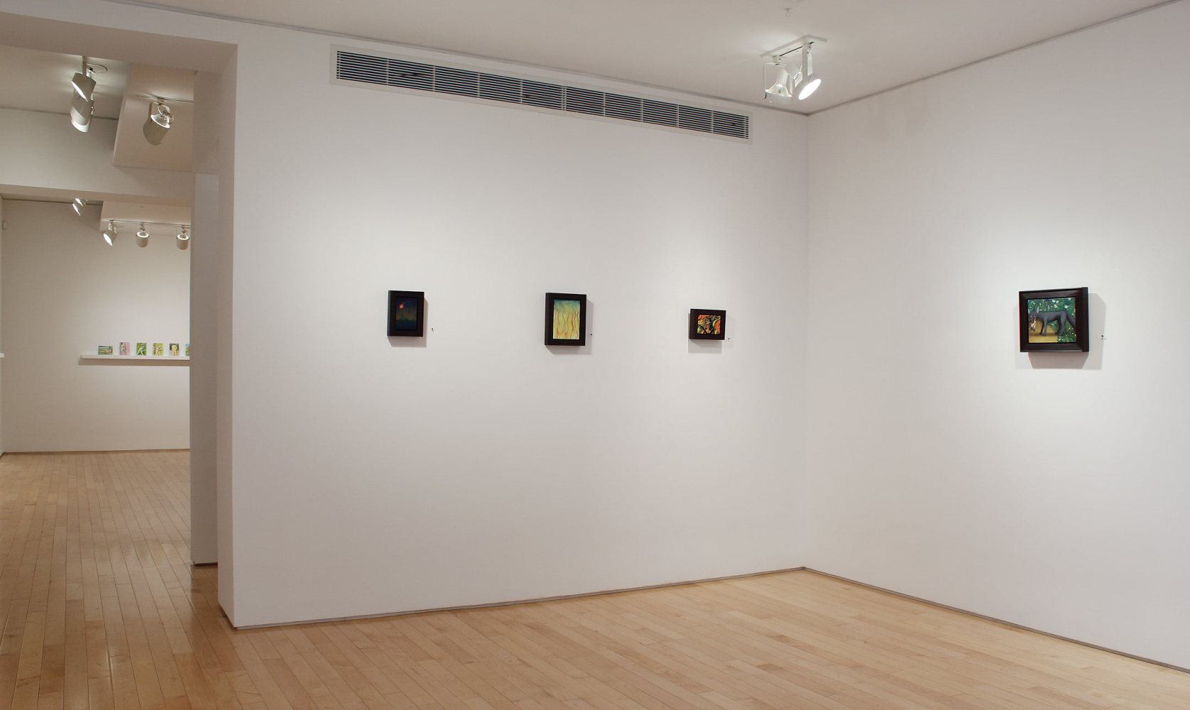 Photograph showing corner view of an exhibition space with four small paintings hanging on white walls