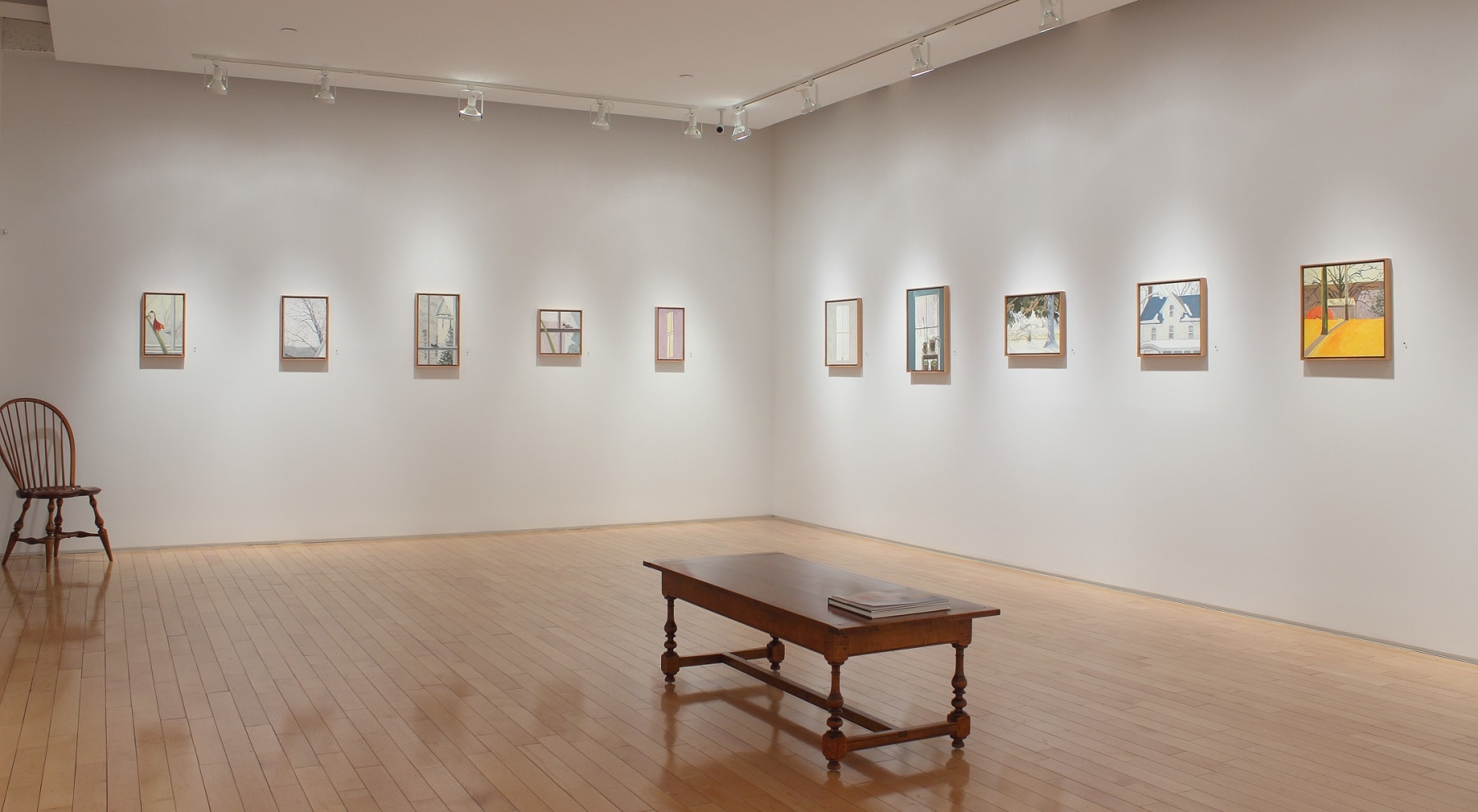 Photograph showing a corner view of an exhibition space, with eleven small paintings hanging on white walls