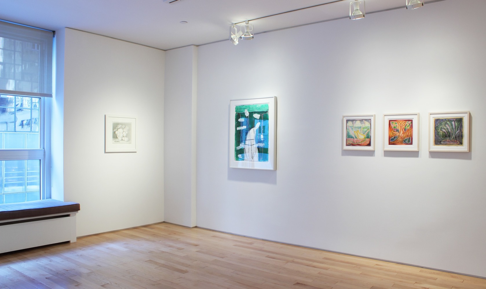 Photograph showing a corner view of an exhibition space, with five framed drawings hanging on white walls
