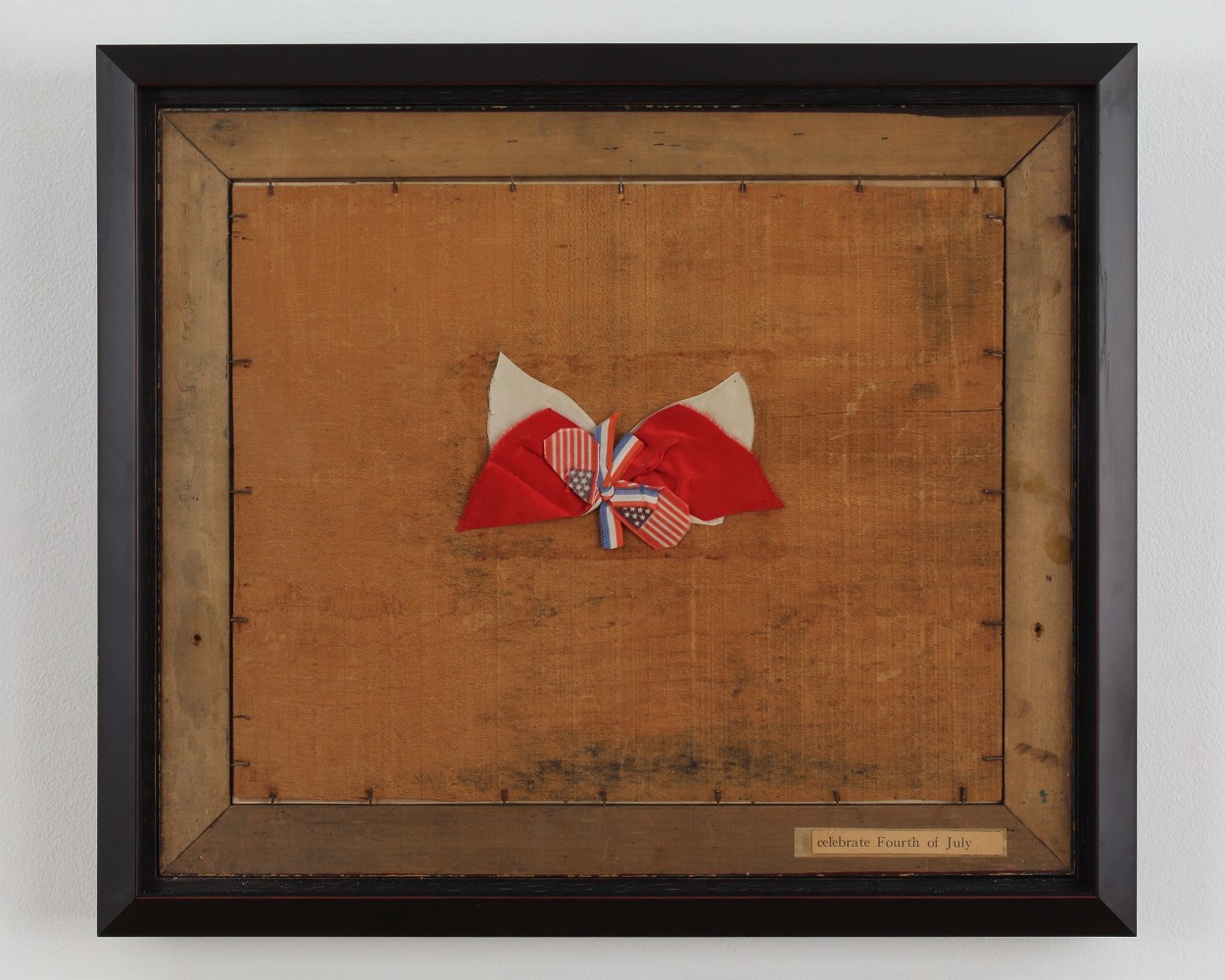 Framed collage with pieces of cloth in red, white and blue tied in a bow on a brown wooden surface and a cut out piece of text on the bottom right that reads &quot;celebrate Fourth of July&quot;