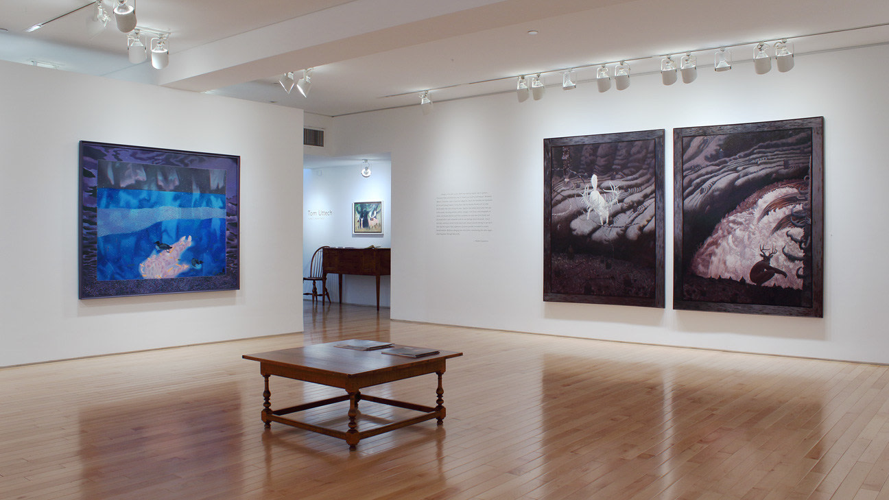 Photograph showing a corner view of an exhibition space with four paintings hanging on white walls