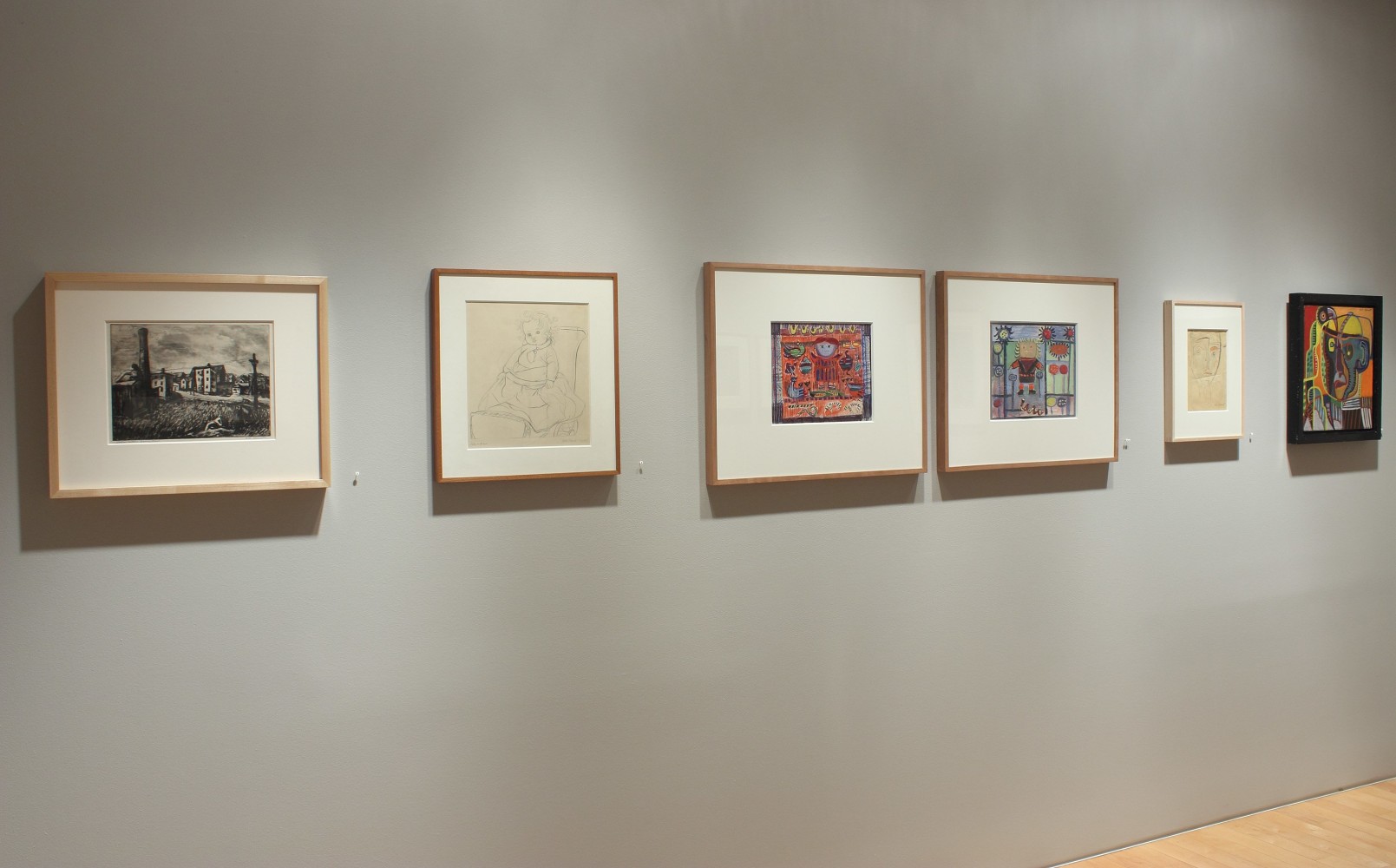 Photograph showing a view of an exhibition space with six framed drawings hanging on a wall