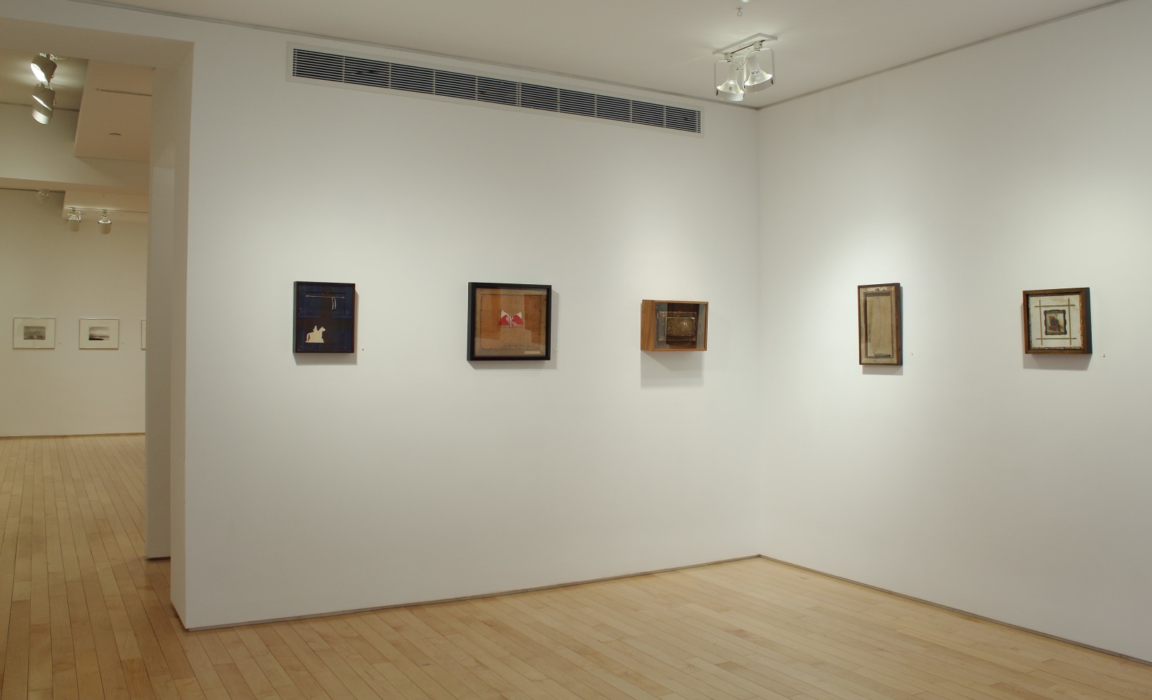 Photograph showing a corner view of an exhibition space with five paintings hanging on white walls