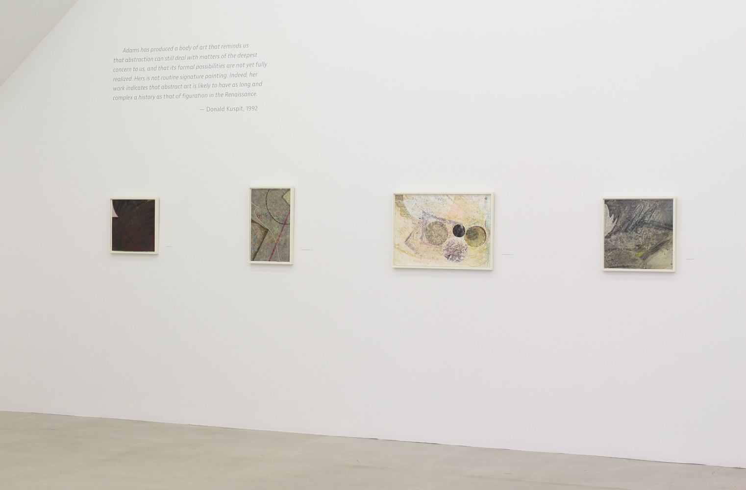 Photograph showing a view of an exhibition space, with four paintings hanging on a white wall