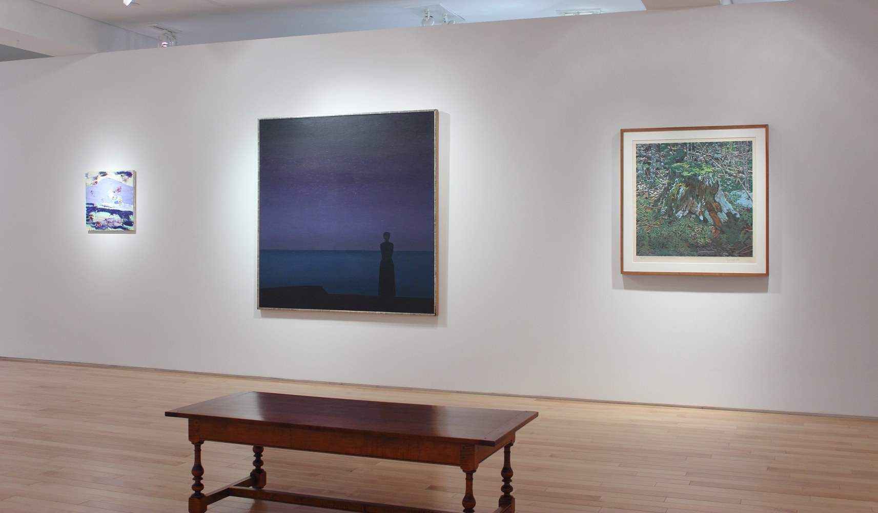 Photograph showing a view of an exhibition space, with one large painting and two smaller paintings hanging on a white wall