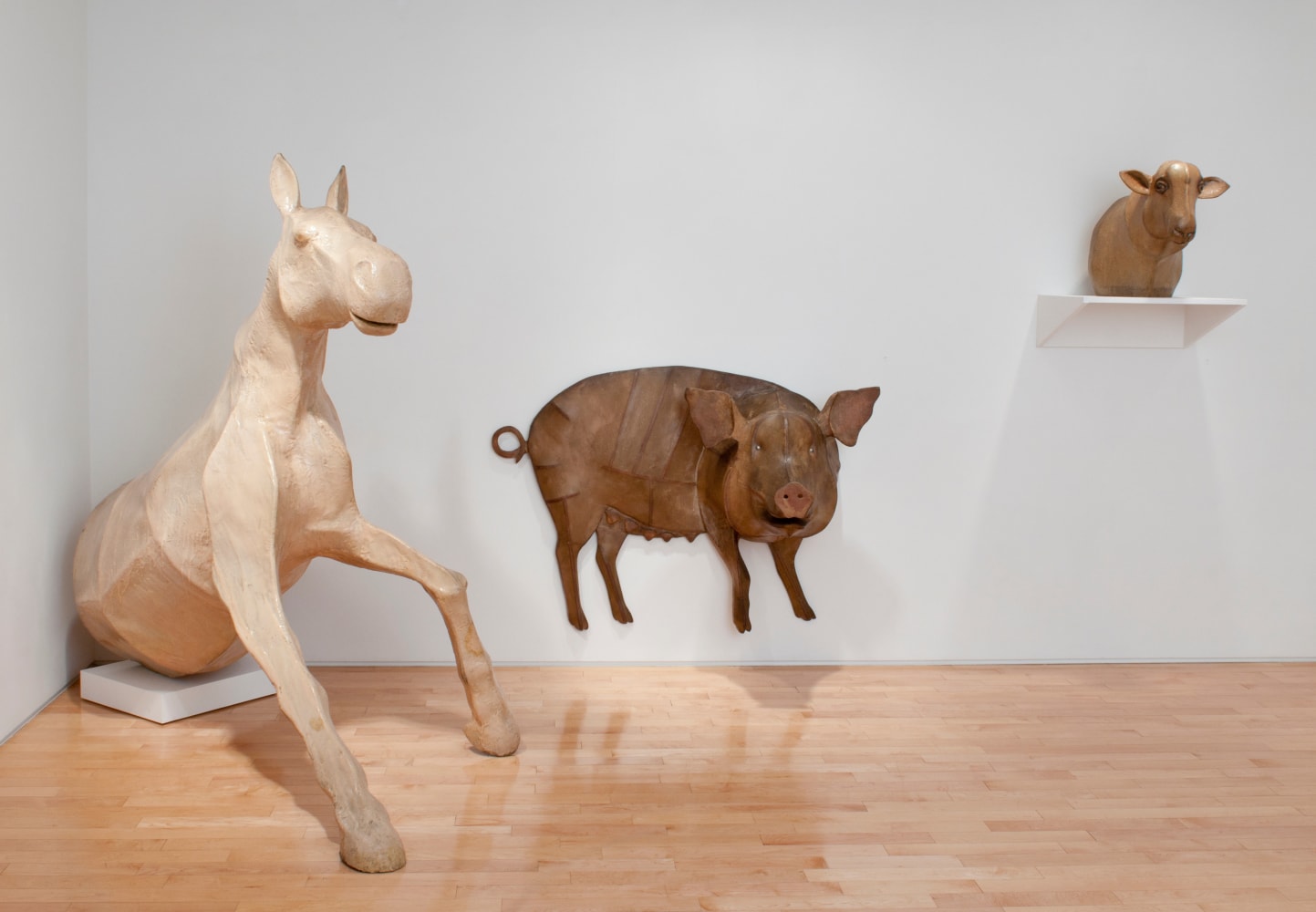 Photograph showing a view of an exhibition space, with a large sculpture emerging from the corner, one hanging on the wall, and a third on a shelf on the wall