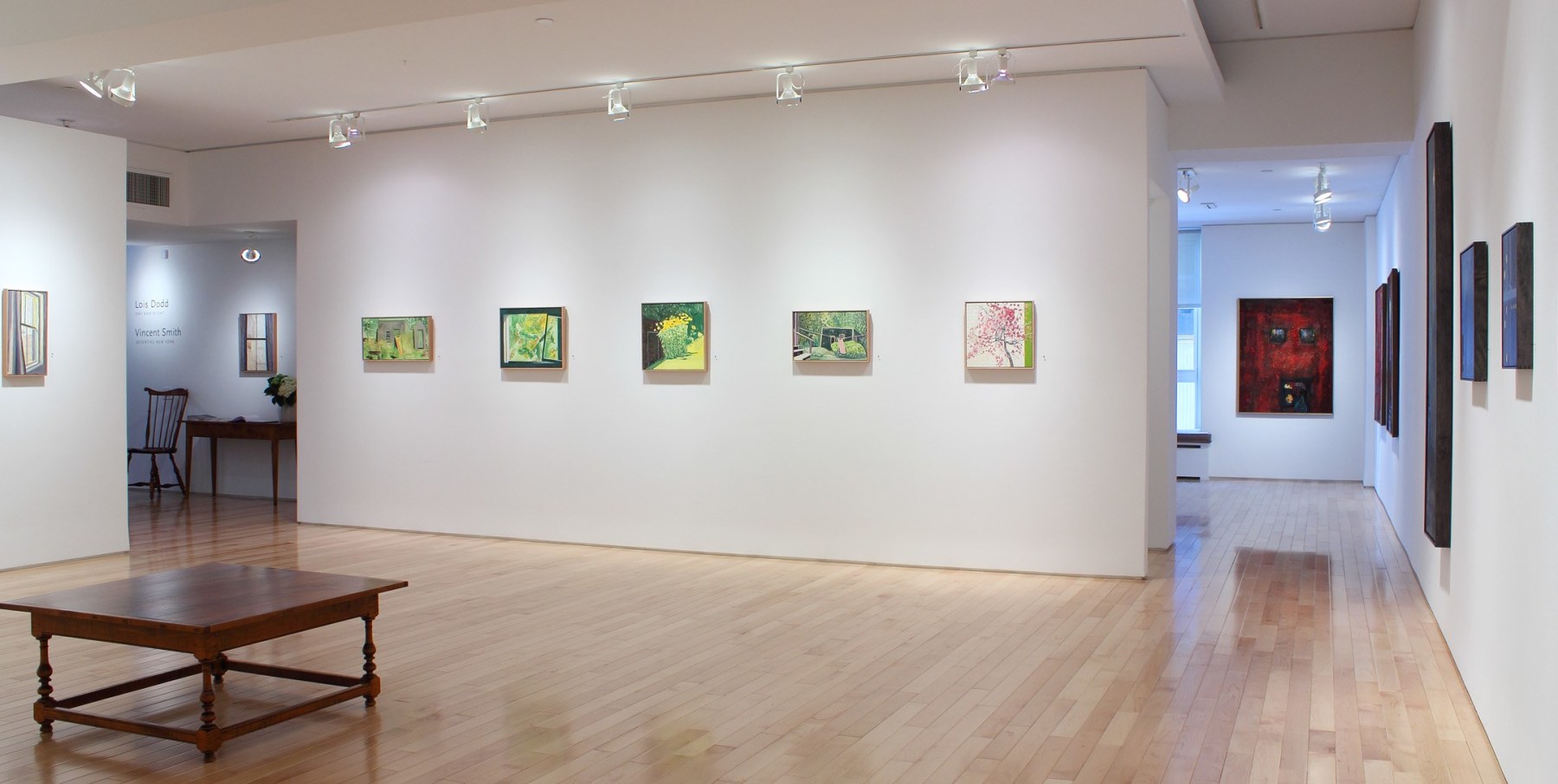 Photograph showing corner view of an exhibition space, with six painting hanging on white walls