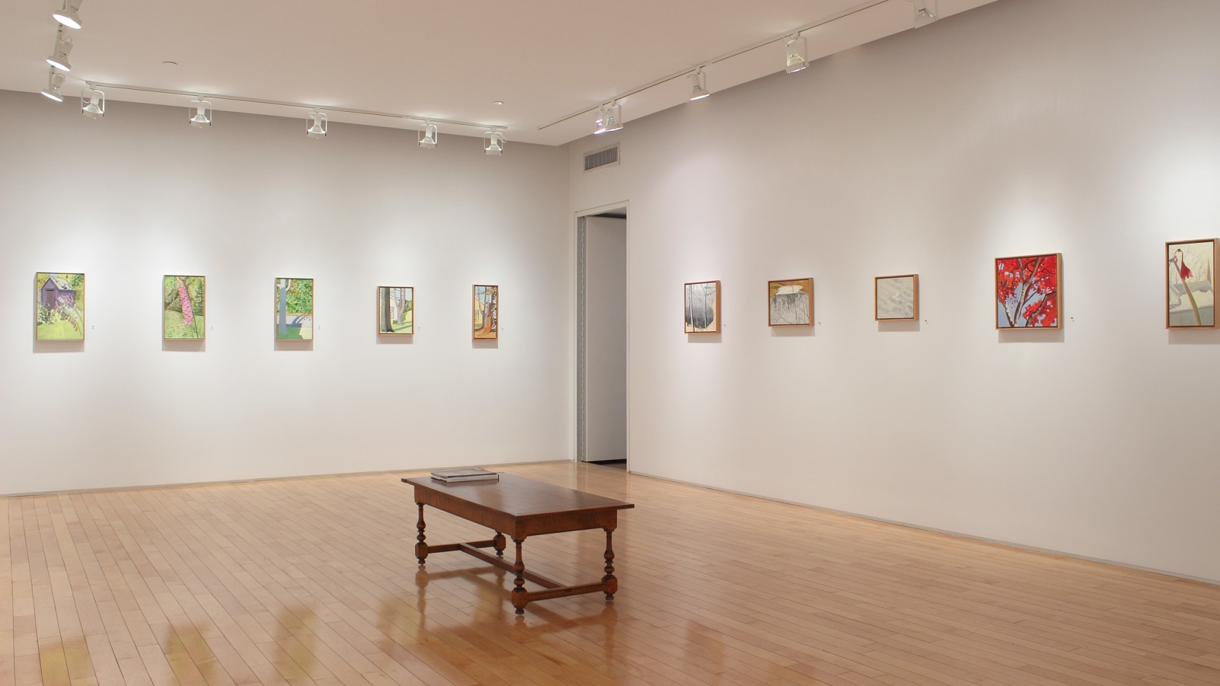 Photograph showing a corner view of an exhibition space, with ten small paintings hanging on white walls