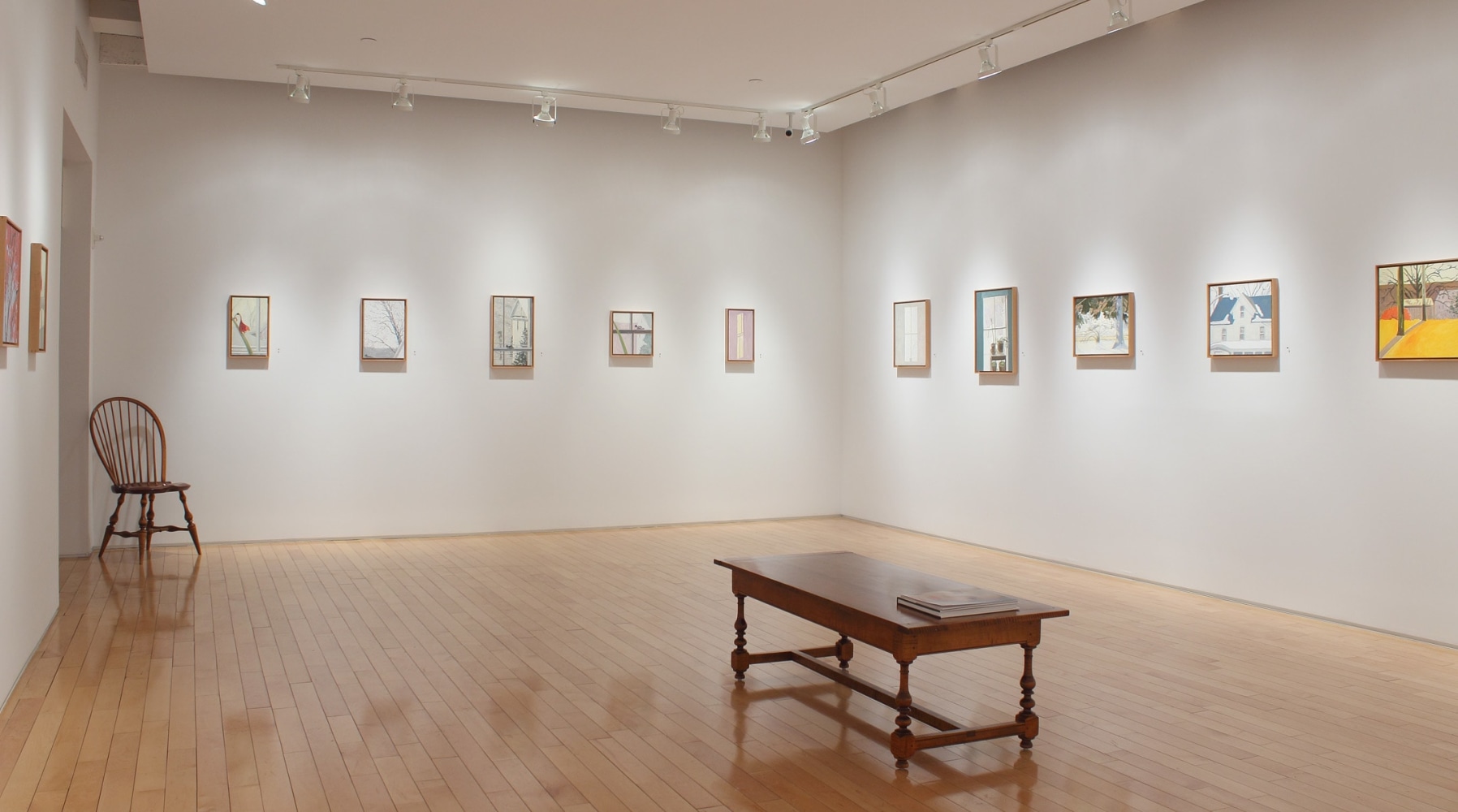 Photograph showing a corner view of an exhibition space, with eleven small paintings hanging on white walls