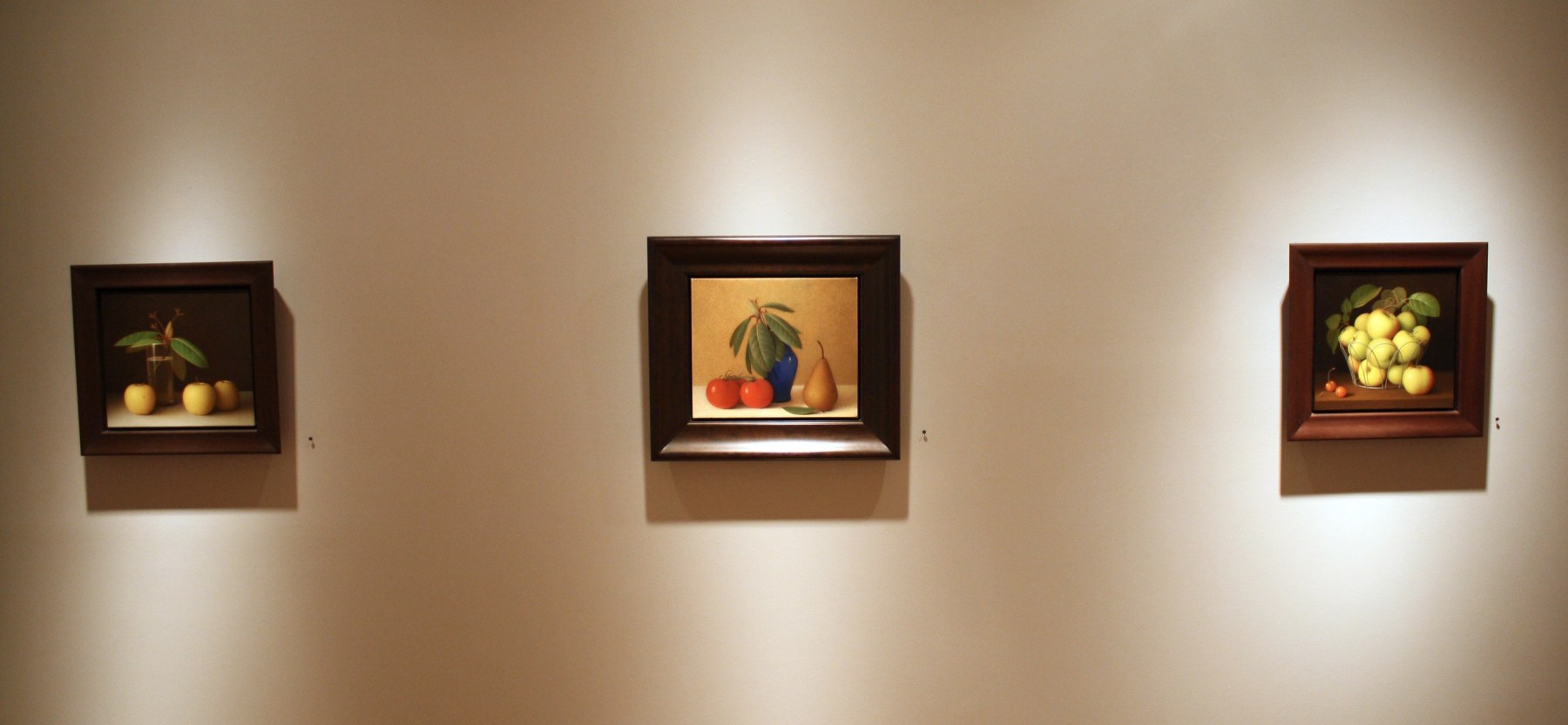 Photograph showing a view of an exhibition, with three small framed paintings hanging on a wall