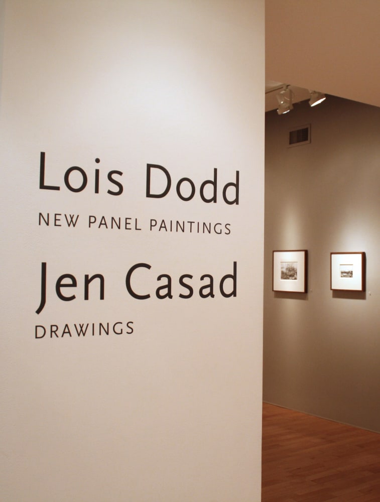 Photograph showing a view of an exhibition space, with two pieces of wall text; one reading &quot;Lois Dodd: New Panel Paintings&quot; and the other reading &quot;Jen Casad: Drawings,&quot; with two small framed drawings in the background