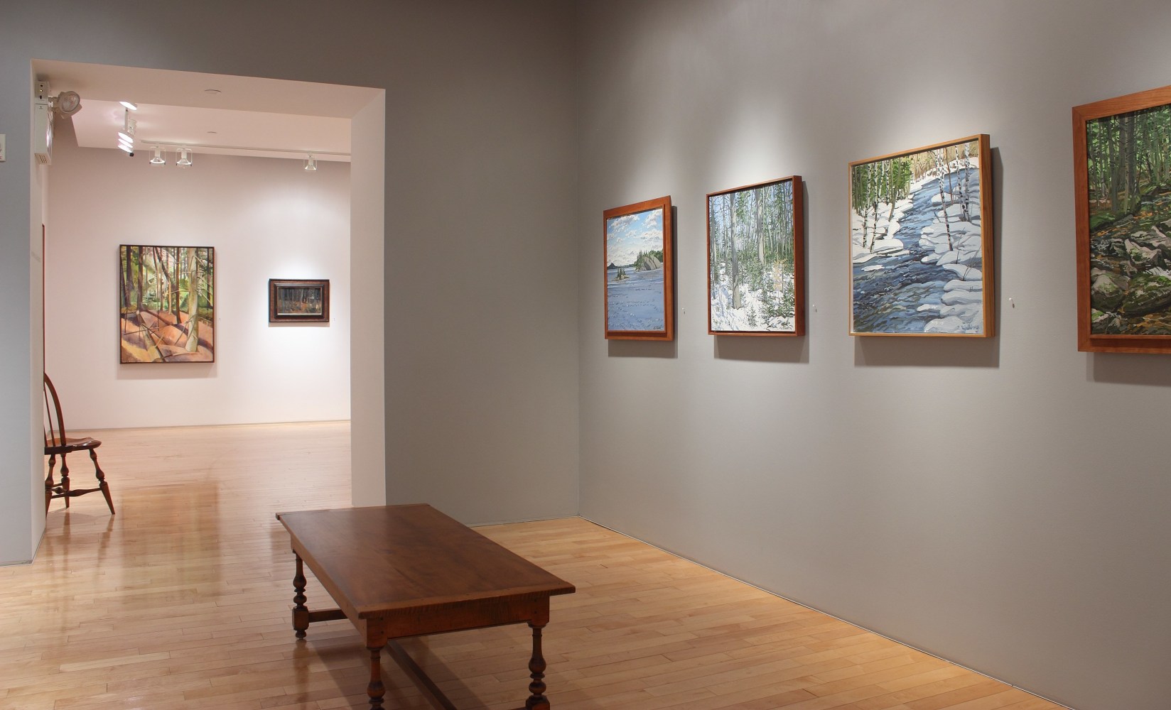 Photograph showing a view of an exhibition space with four framed paintings hanging on a wall