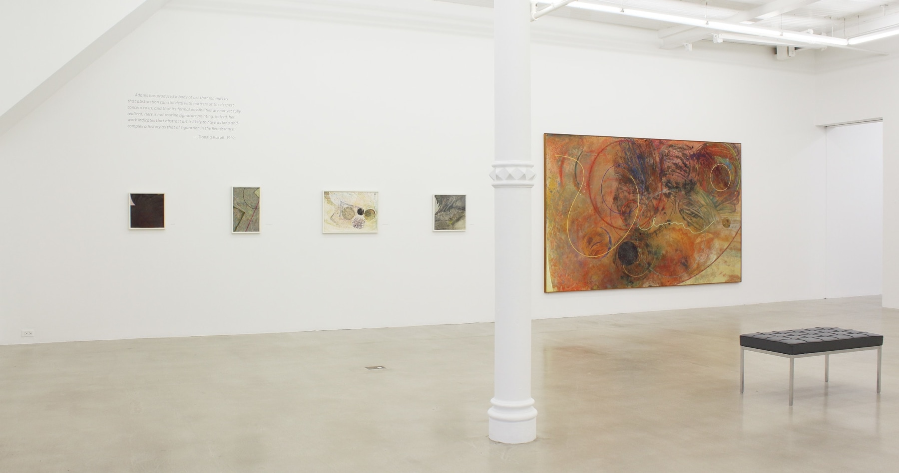 Photograph showing a view of an exhibition space, with five paintings hanging on a white wall