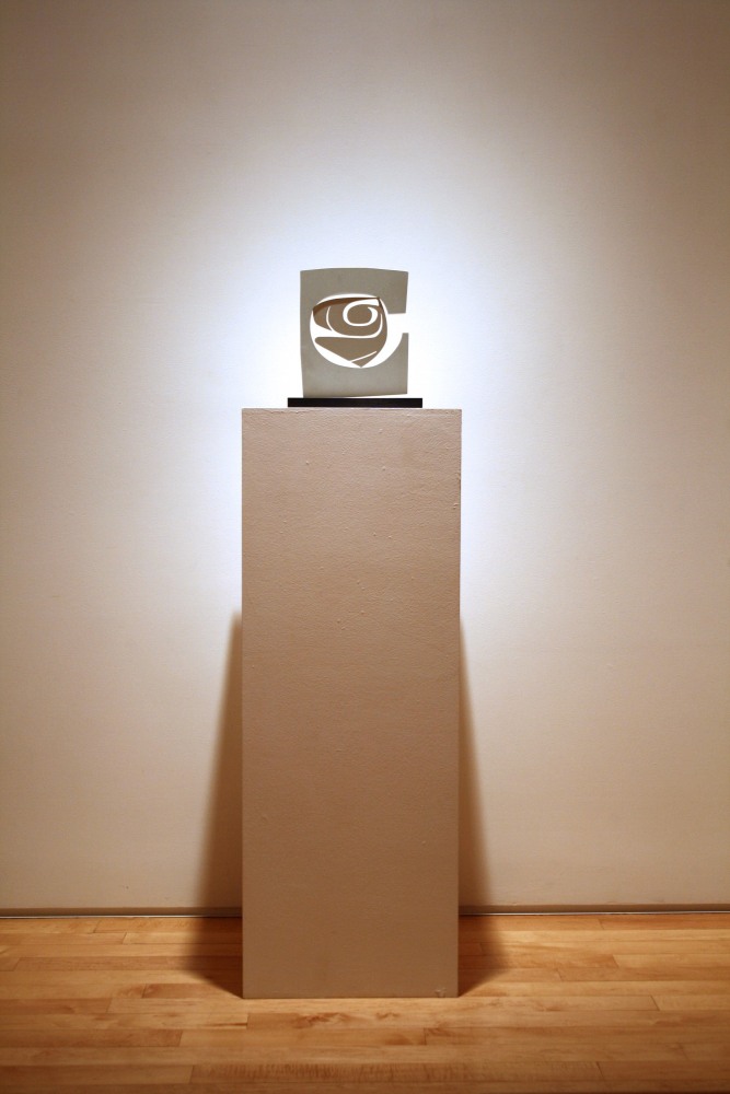 Photograph showing a view of an exhibition, with a small sculpture on top of a pedestal