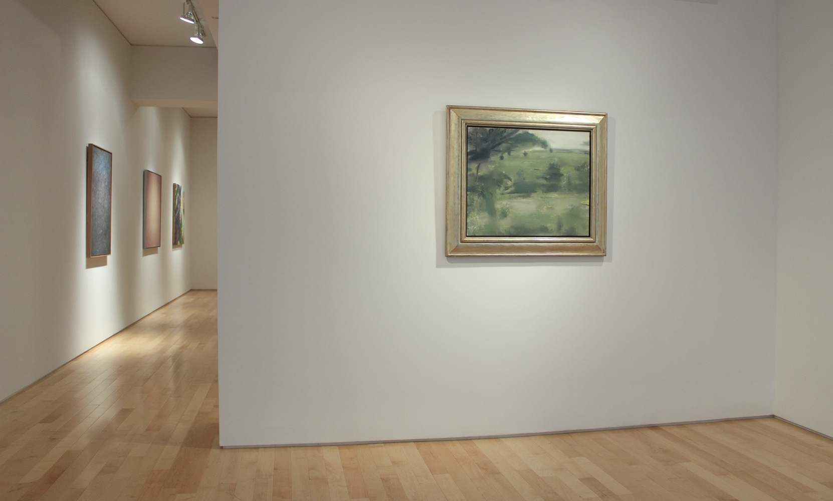 Photograph showing a view of an exhibition space with one painting hanging on a white wall