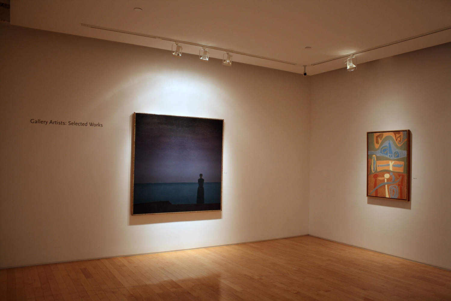 Photograph showing a corner view of an exhibition space, with two paintings hanging on a white wall