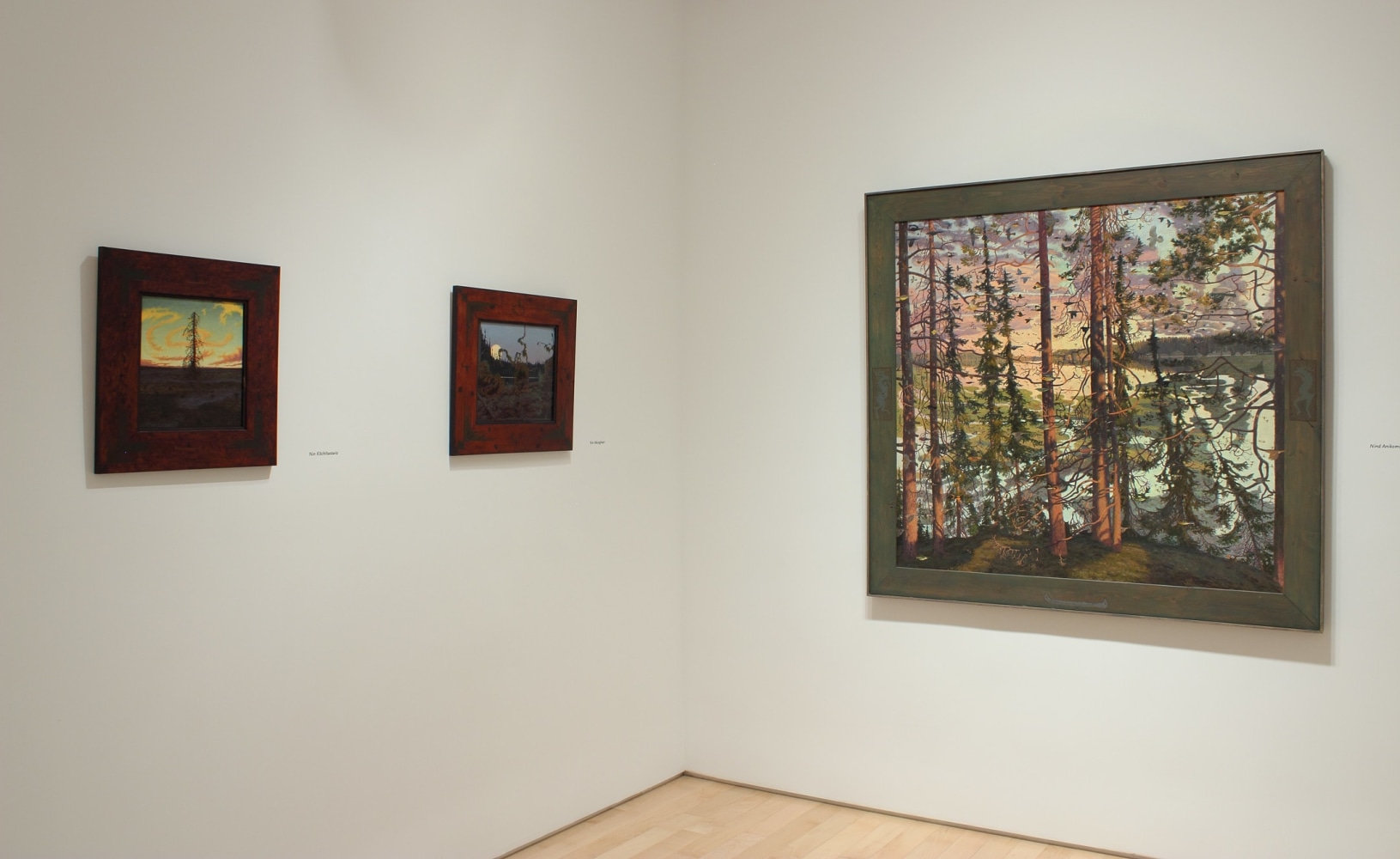 Photograph showing a corner view of an exhibition space, with three paintings hanging on white walls