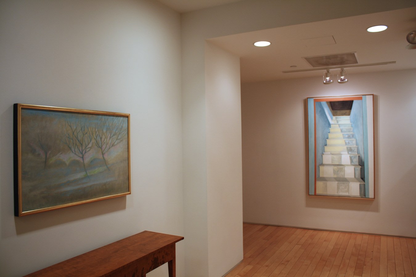 Photograph showing a view of an exhibition space, with two framed paintings hanging on white walls