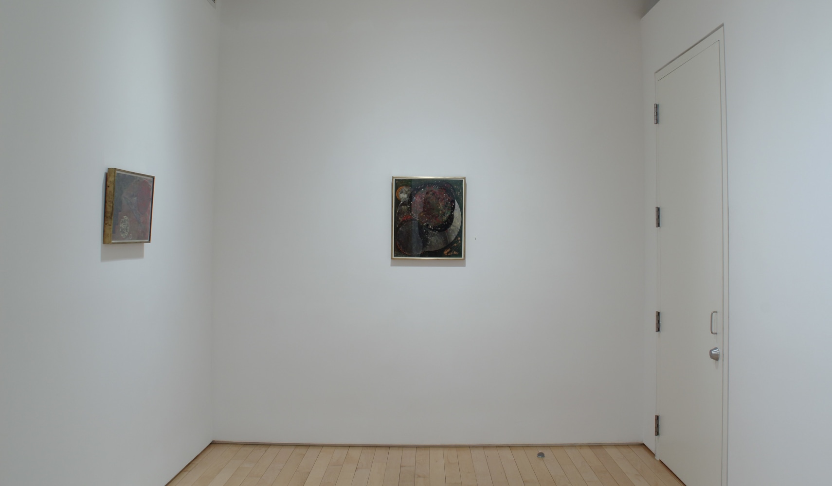 Photograph showing a corner view of an exhibition space, with two small paintings hung on white walls
