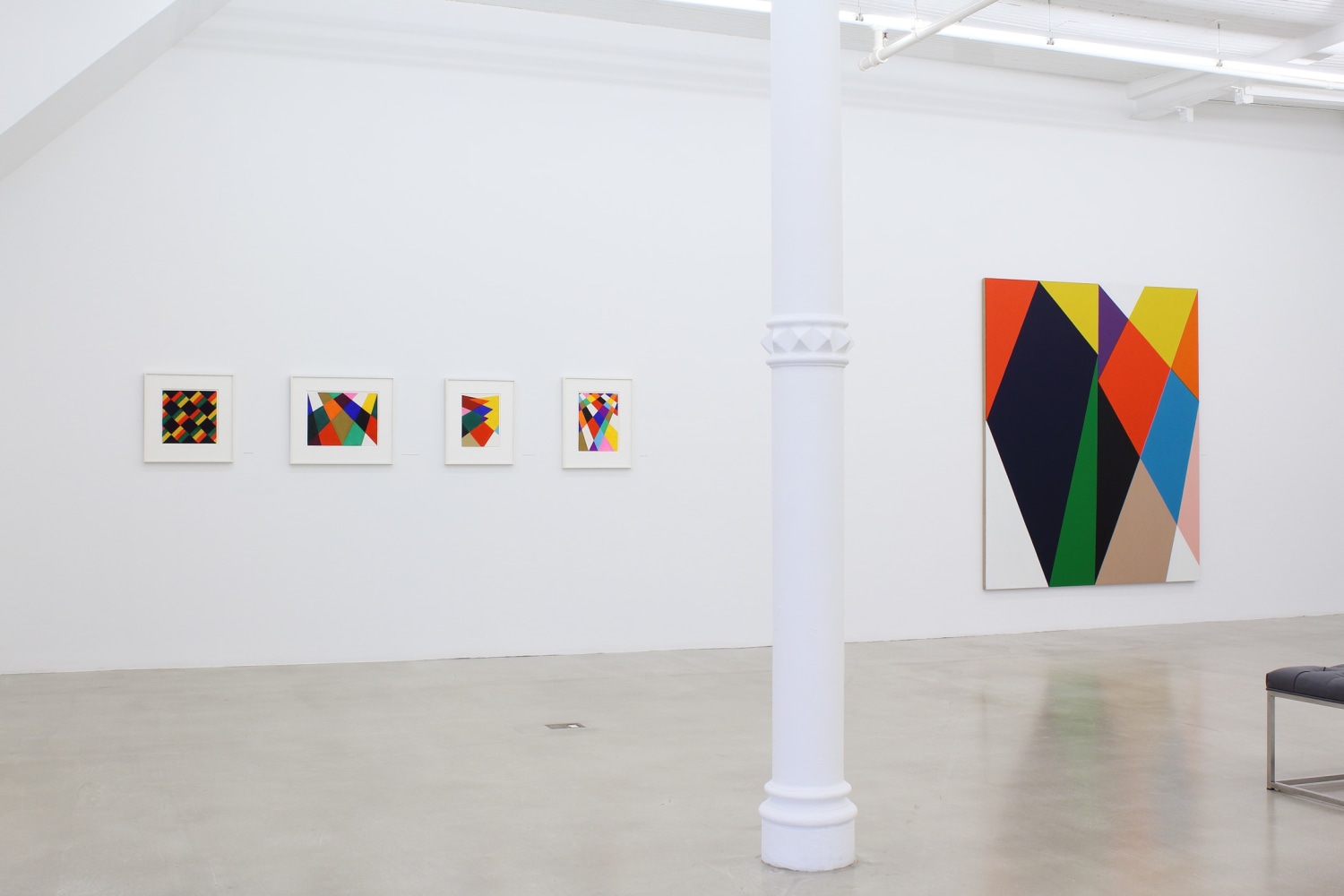 Photograph showing a view of an exhibition space, with five paintings hanging on a white wall