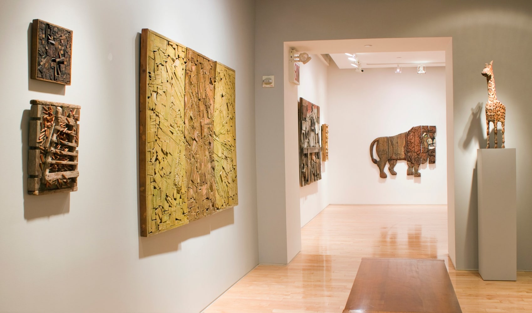 Photograph showing a view of an exhibition space, with six sculptures hanging on the walls and one sculpture on a pedestal to the right