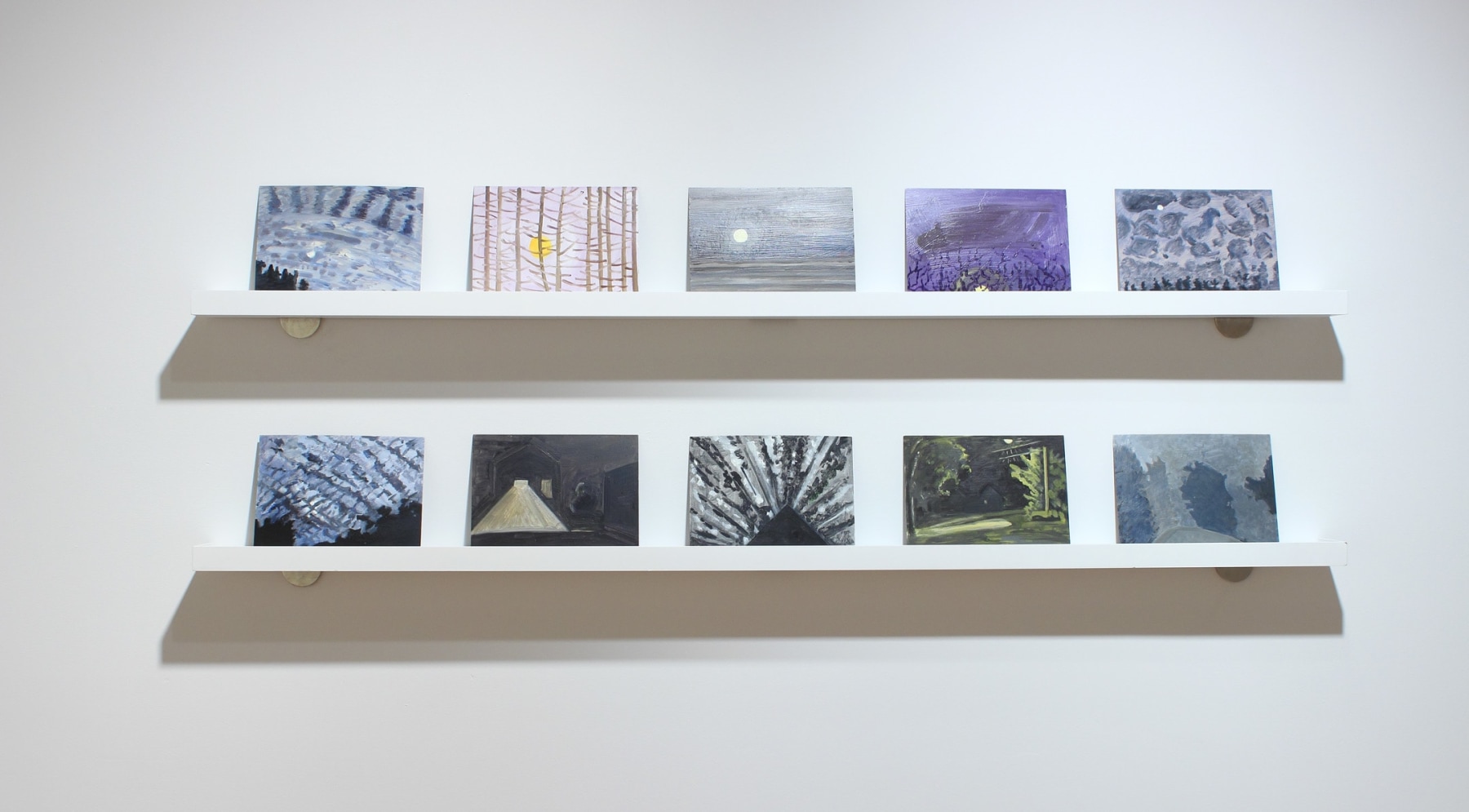 Photograph showing a detail of an exhibition, with two shelves containing ten small paintings